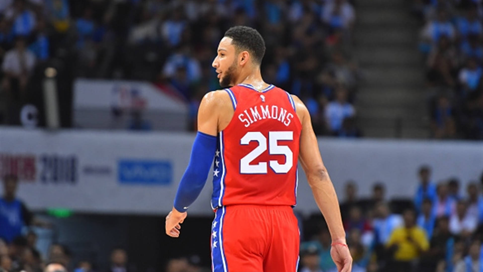 本·西蒙斯背影紅衣照 壁紙 — 籃球運動員 Ben Simmons 身穿紅藍球衣 25 號，在球場上背對鏡頭走開，背景有觀眾。