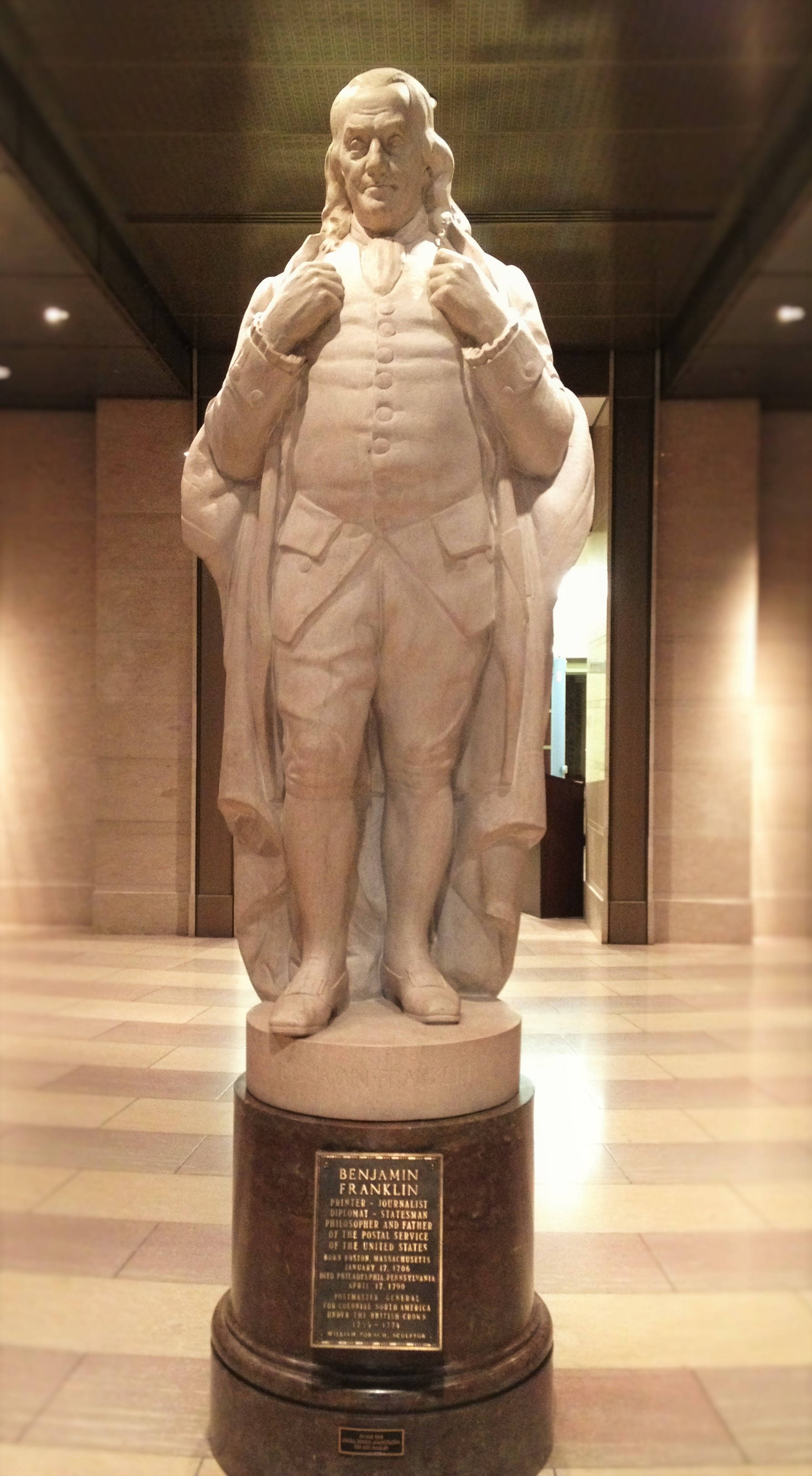 本傑明·富蘭克林全身大理石雕像 壁紙 — 本傑明·富蘭克林的大理石雕像自豪地矗立在一個宏偉、燈光溫暖的博物館走廊中的深色基座上，走廊舖有瓷磚地板和高大的柱子。