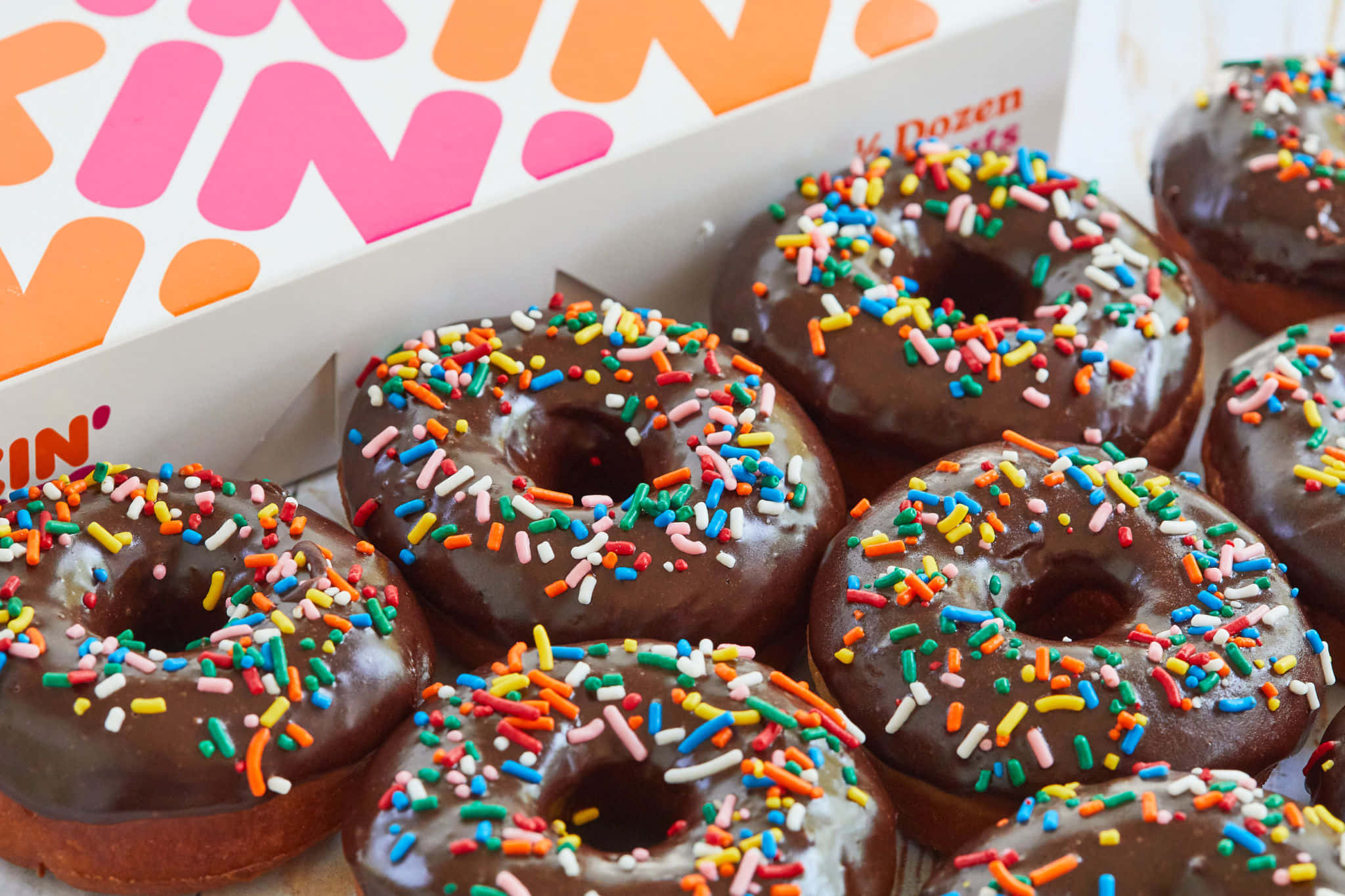Glazed Donut 桌布 壁紙 — 朱古力糖霜冬甩上面灑滿彩色糖針，從品牌盒子中傾瀉而出的特寫。