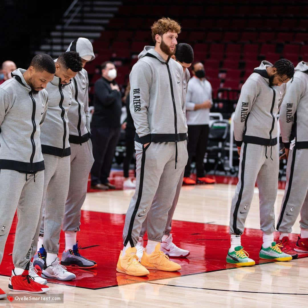 朱斯·努爾基奇與隊友賽前禱告 壁紙 — 籃球運動員穿著灰色 Blazers 熱身裝備，在紅色和木質球場上莊嚴地低頭站立。