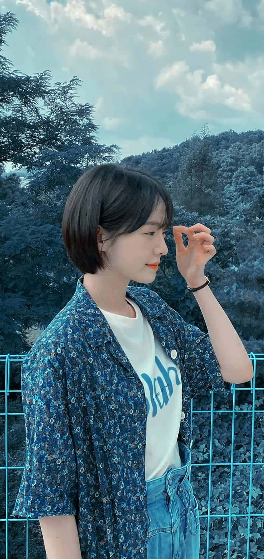 年輕女子穿著藍色花卉襯衫站在森林地區的圍欄旁