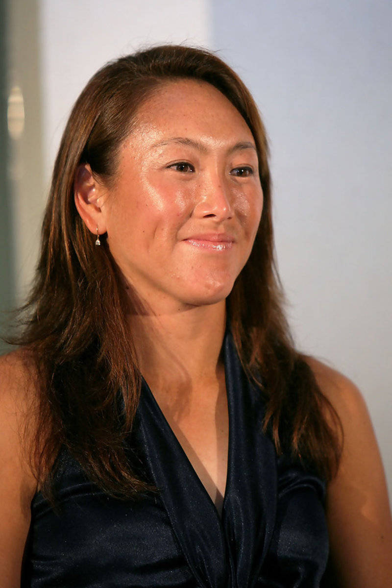 一位長長棕色頭髮的女性穿著深藍色緞面上衣，溫柔地微笑。