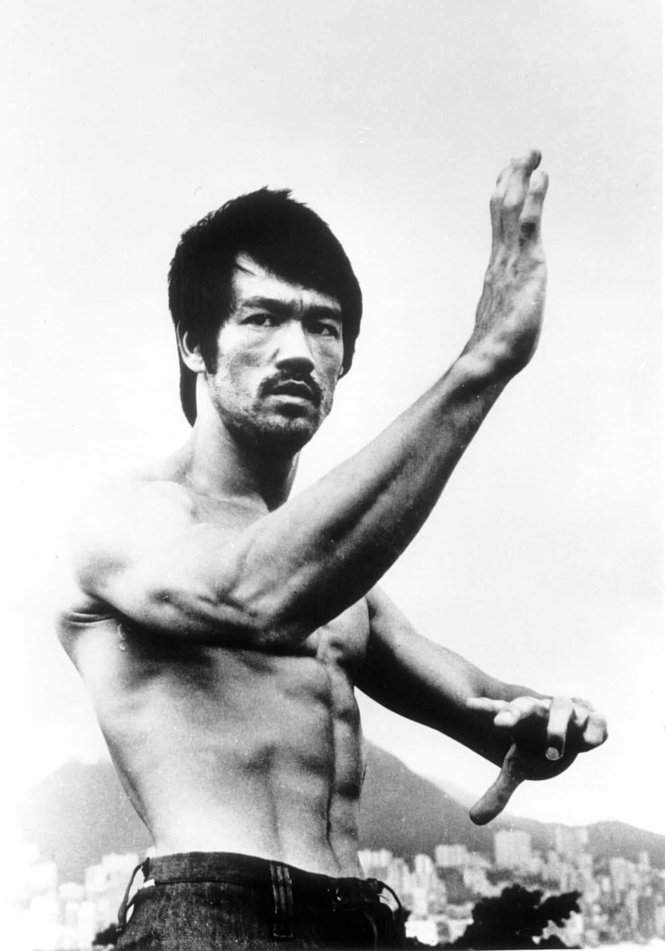 李小龍赤裸上身擺出武術姿勢，身後是城市天際線。 — 李小龍 壁紙