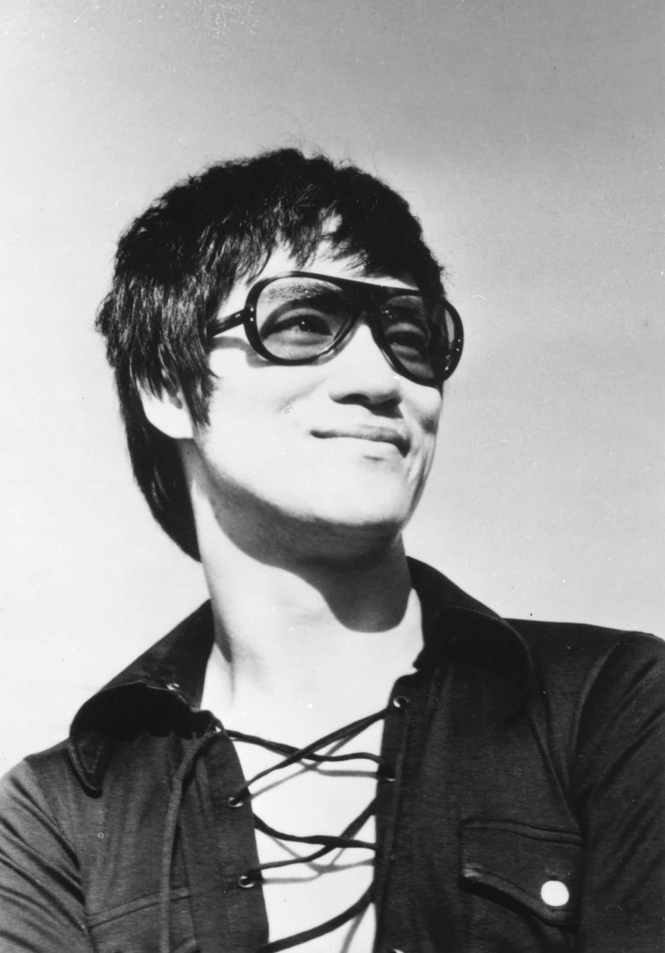 李小龍戴住太陽眼鏡同綁帶恤衫，對住鏡頭微笑。 — 李小龍 壁紙