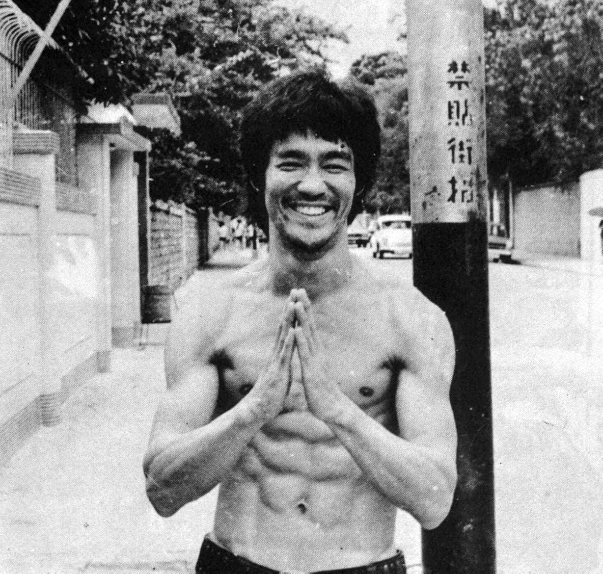 李小龍赤膊雙手合十，在街燈柱前微笑。