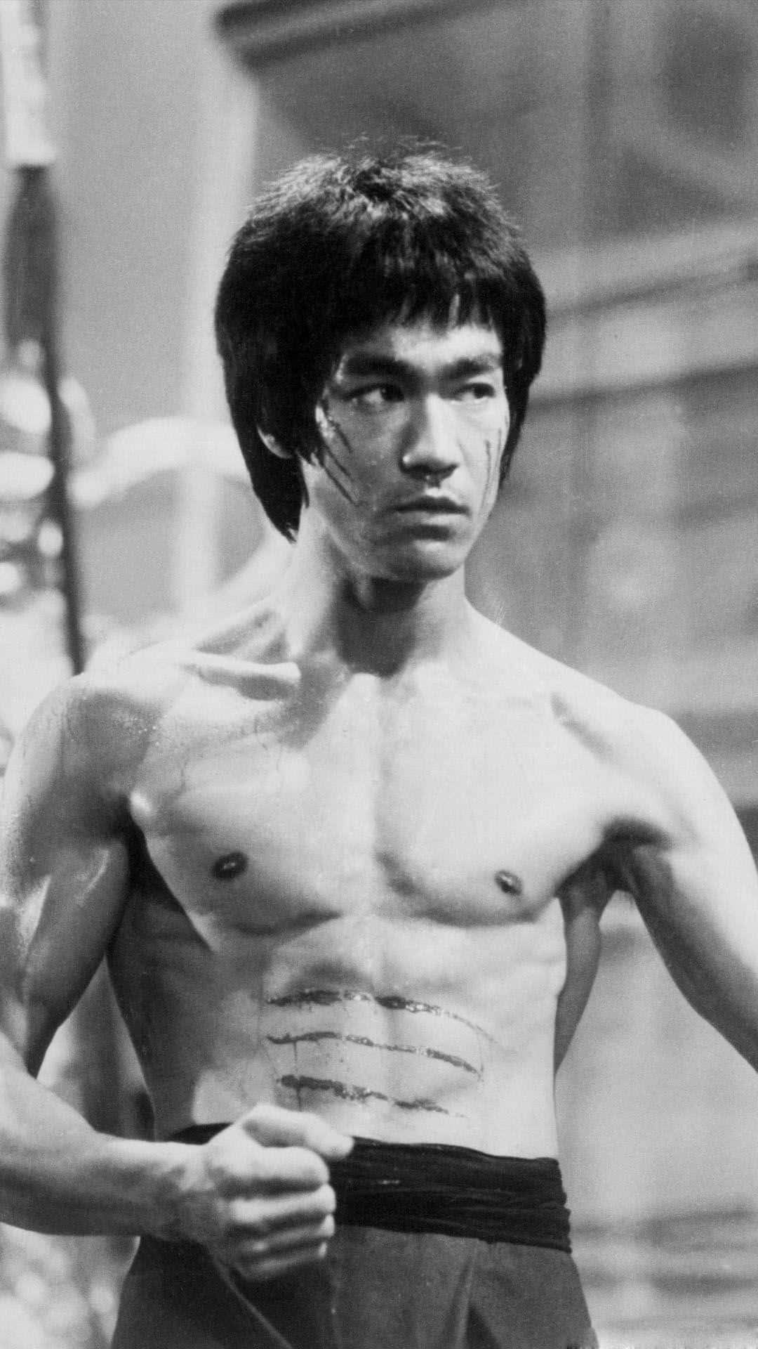 李小龍赤裸上身，臉上和軀幹有傷疤，處於黑白武術場景中。