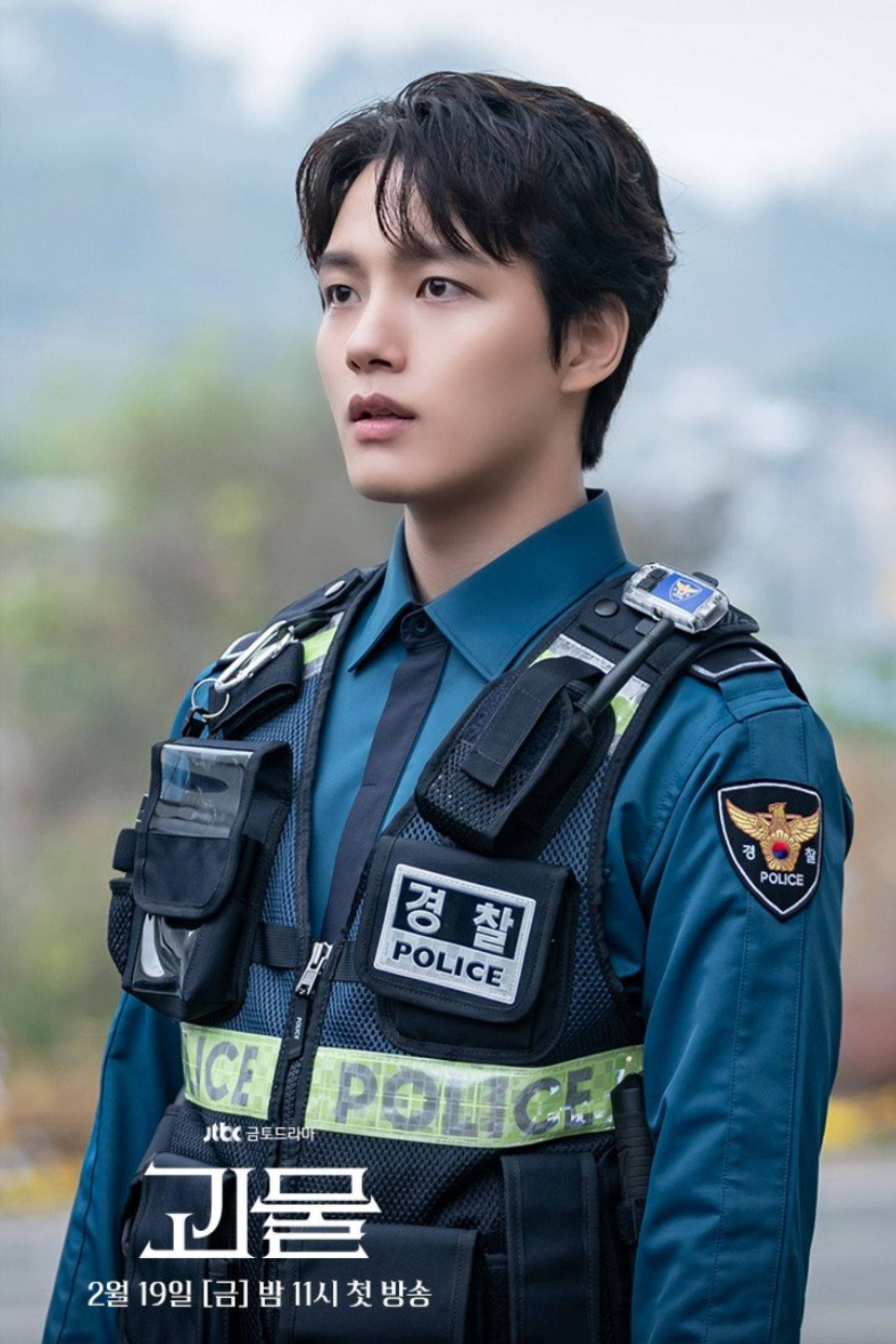 李陣郁警官造型 壁紙 — 一名身穿制服的年輕韓國警察在戶外若有所思地凝視著，背景是煙霧繚繞的山巒。