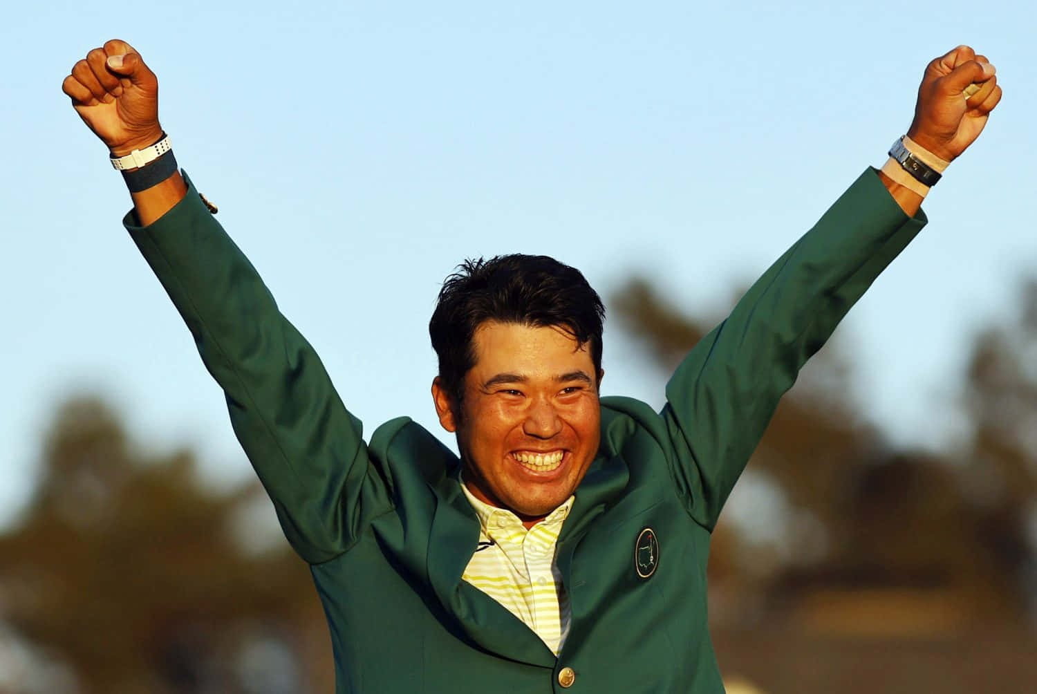高爾夫球手身穿綠色外套舉起雙臂慶祝勝利。