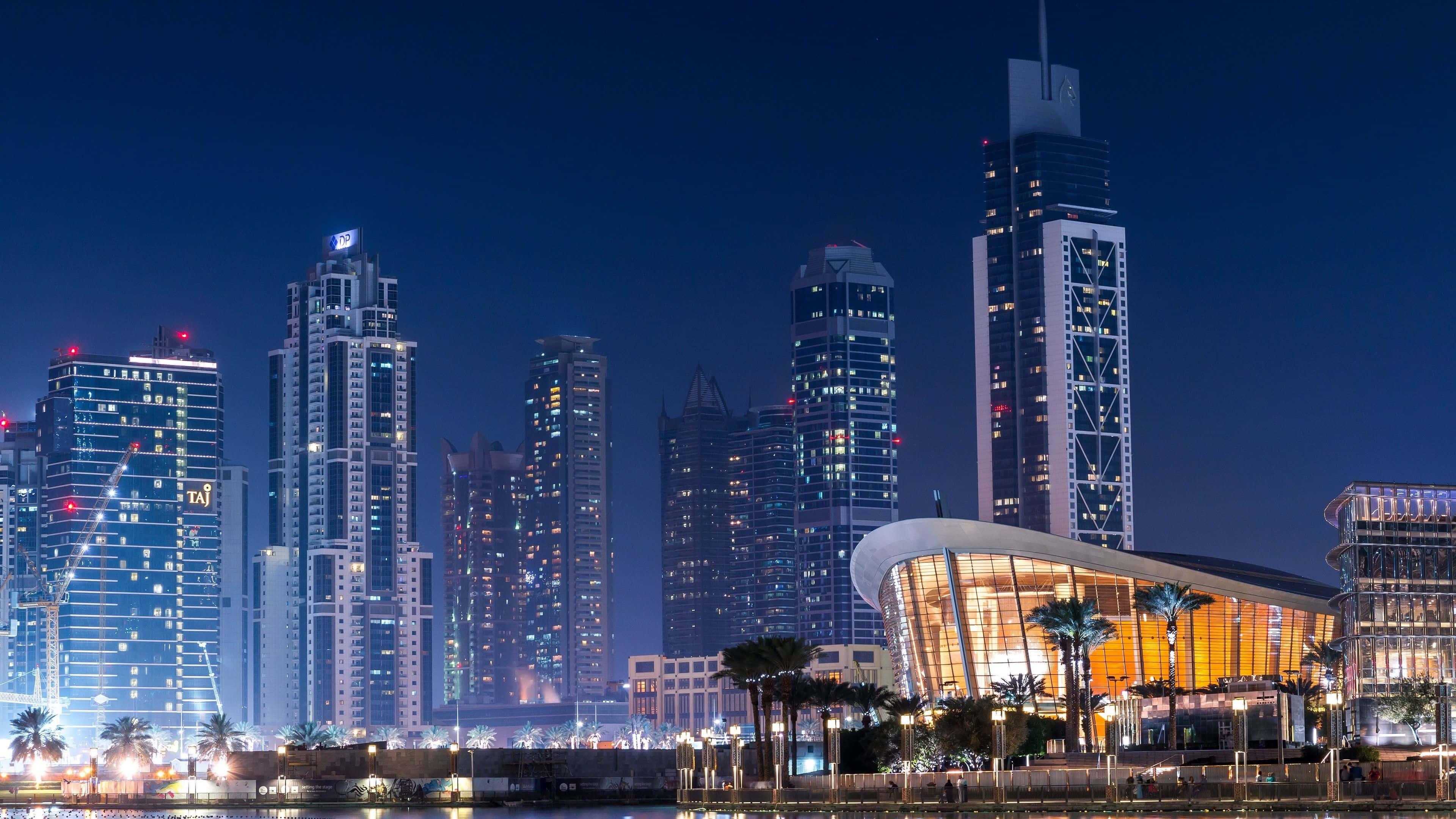 Dubai 桌布 壁紙 — 杜拜令人眼花繚亂的夜景，有燈火通明的摩天大樓和棕櫚樹旁閃閃發光的現代建築。
