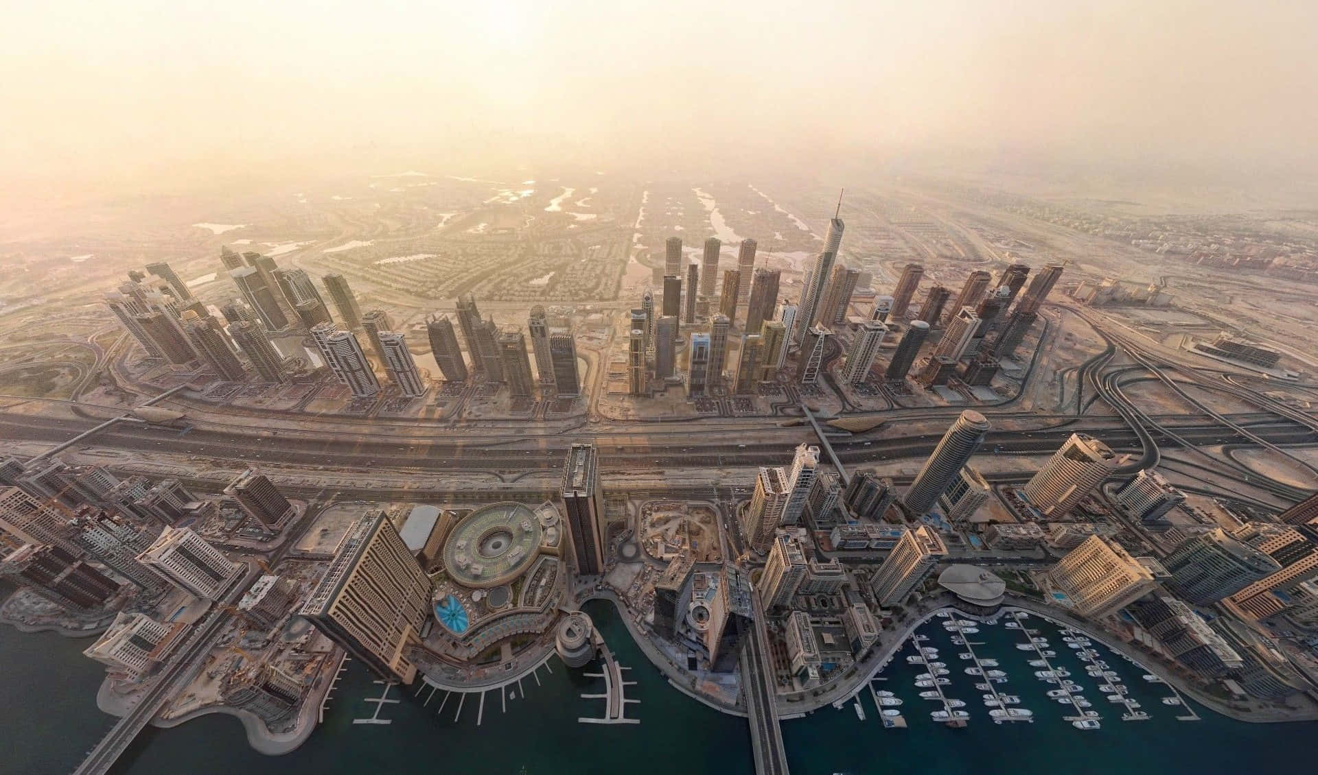 Dubai 桌布 壁紙 — 杜拜天際線在黃金時刻的航拍圖，摩天大樓、碼頭和高速公路沐浴在溫暖的陽光中。