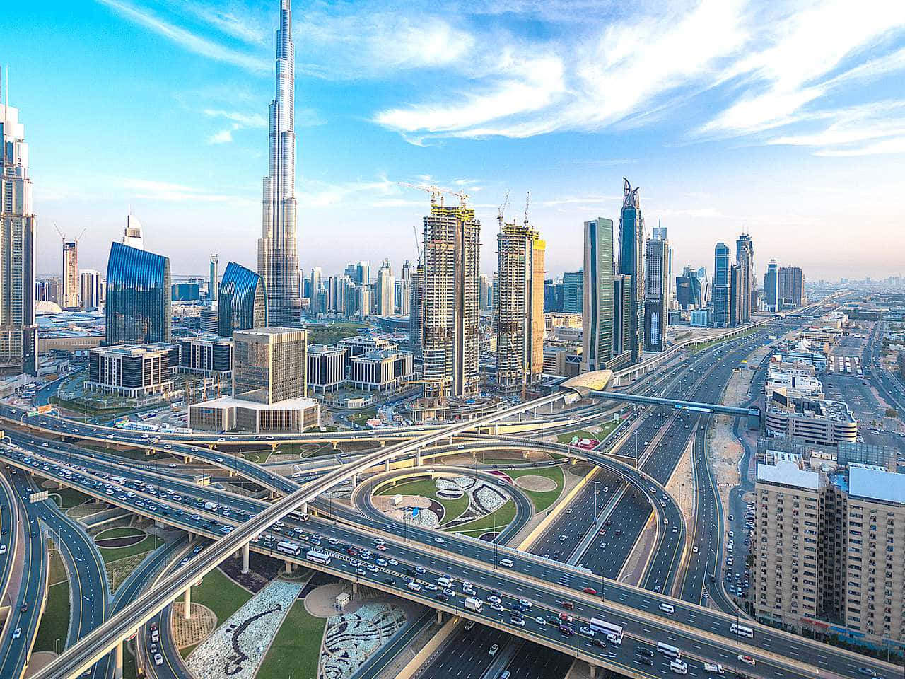 Burj Khalifa 桌布 壁紙 — 杜拜未來主義天際線的航拍圖，在明亮的藍天下，哈利法塔聳立在複雜的高速公路交匯處之上。