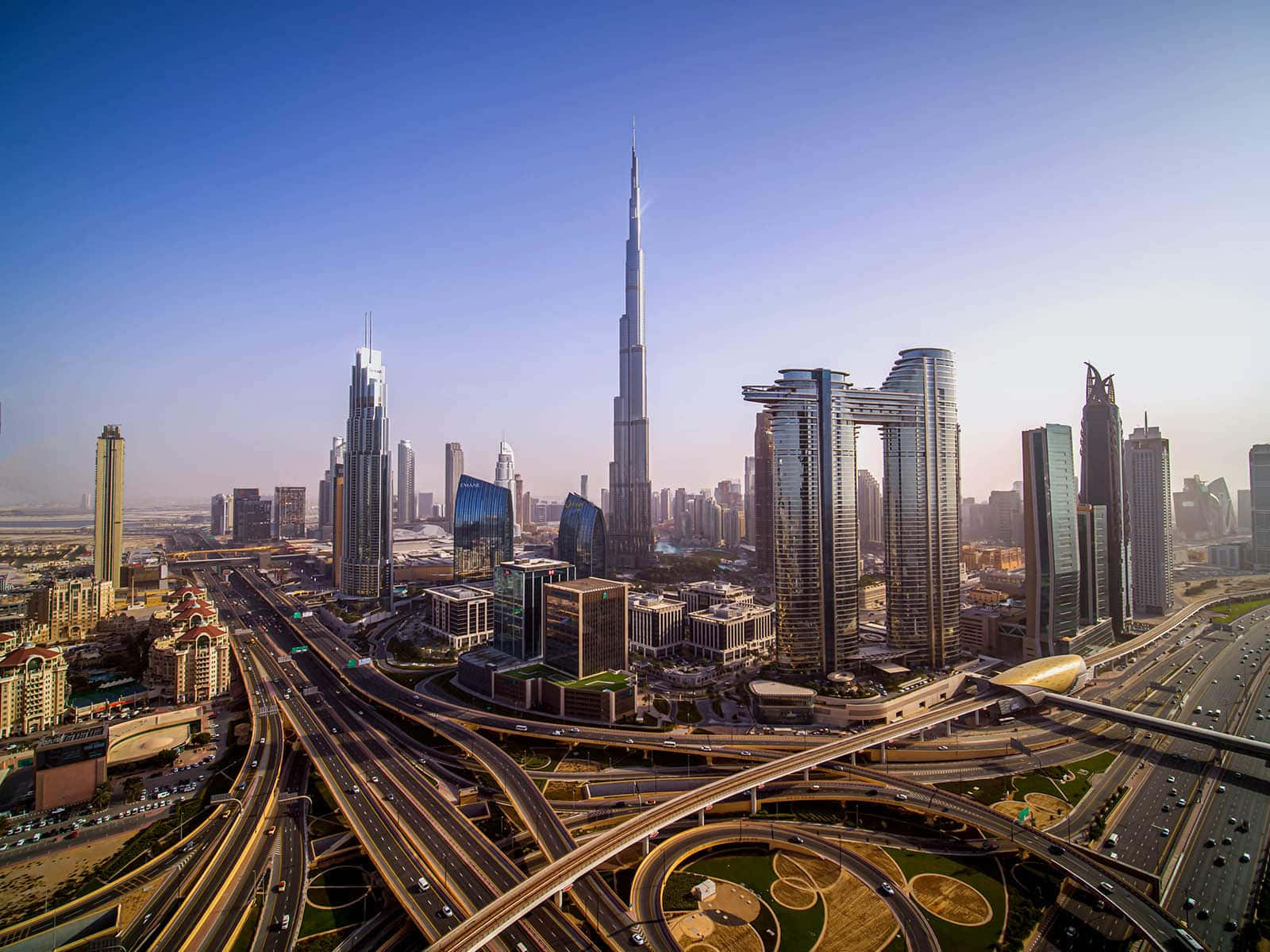 Burj Khalifa 桌布 壁紙 — 杜拜未來主義天際線的鳥瞰圖，以哈利法塔和錯綜複雜的高速公路網絡為主，在晴朗的藍天下。