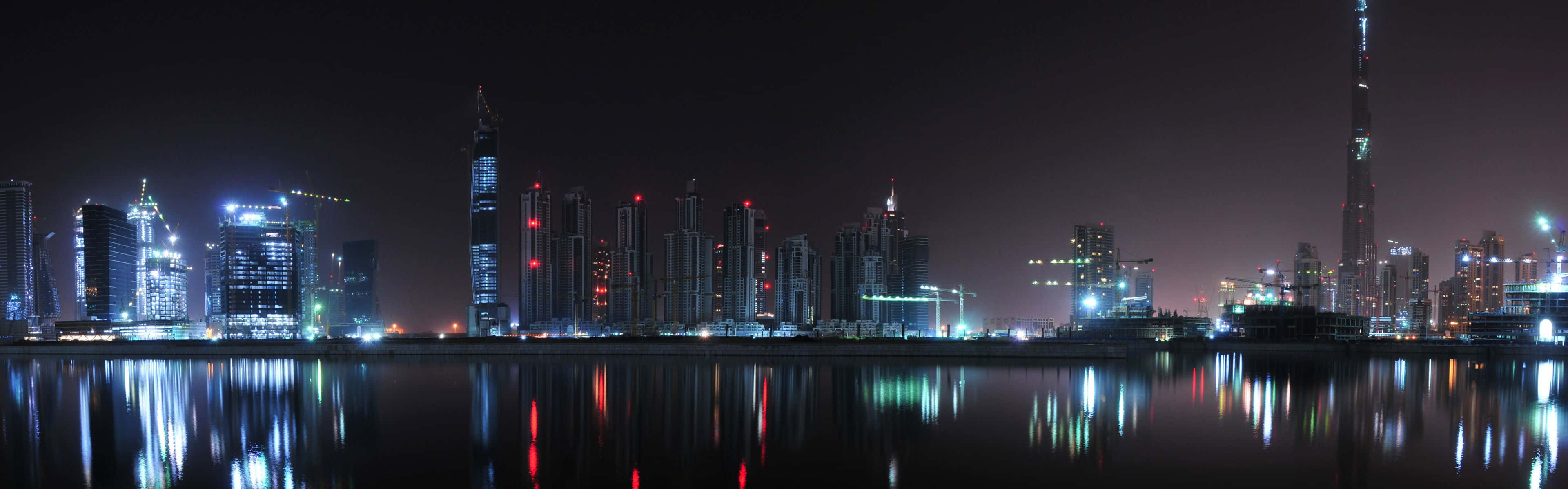 2 Monitor 桌布 壁紙 — 杜拜璀璨天際線的 panoramic 夜景，倒映在平靜水面上，哈利法塔高聳突出。