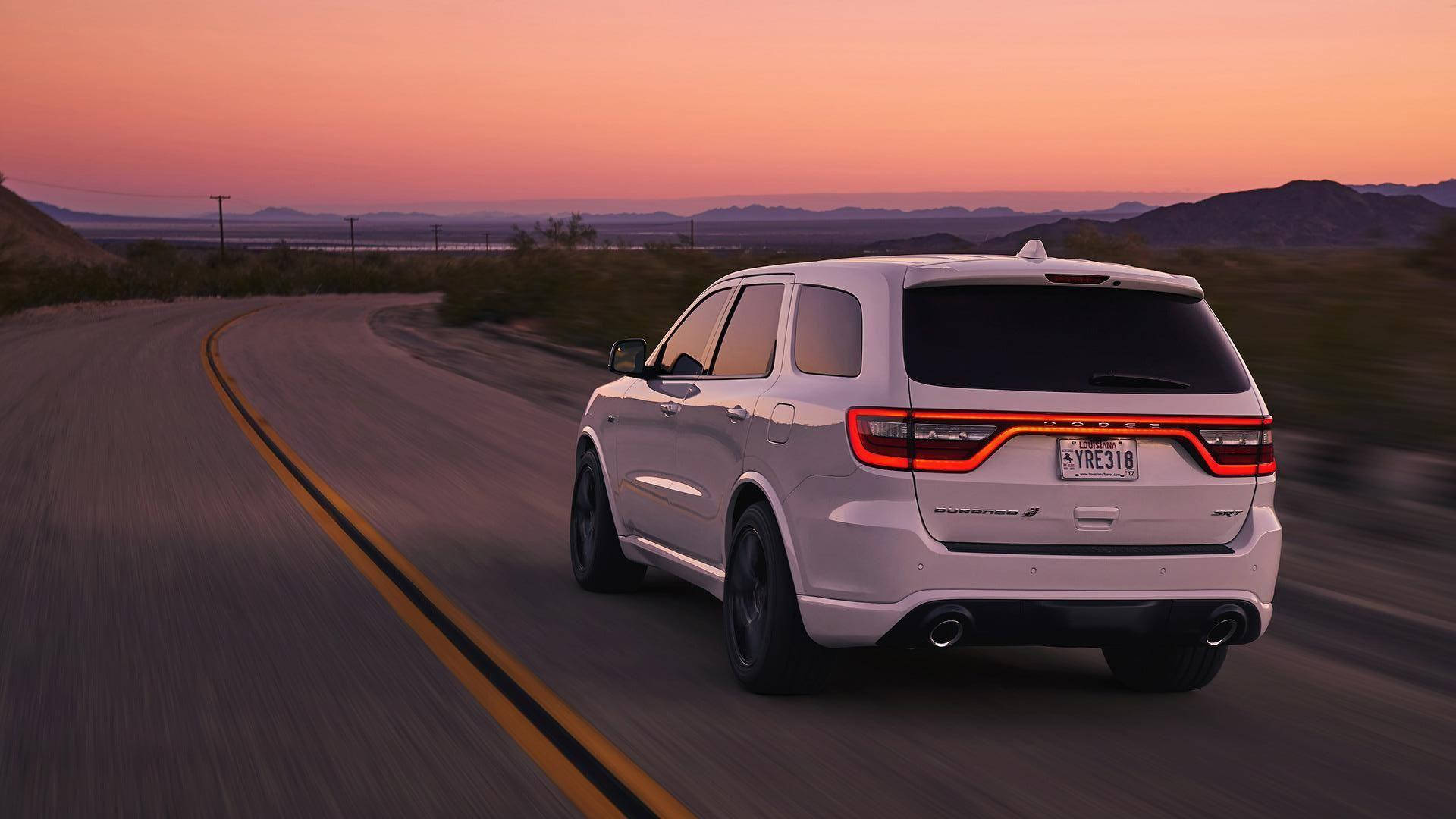 杜蘭戈車輛後視遠景 壁紙 — 一輛白色Dodge Durango SUV在日落時分沿沙漠高速公路飛馳，天空呈現粉紅色和橙色。