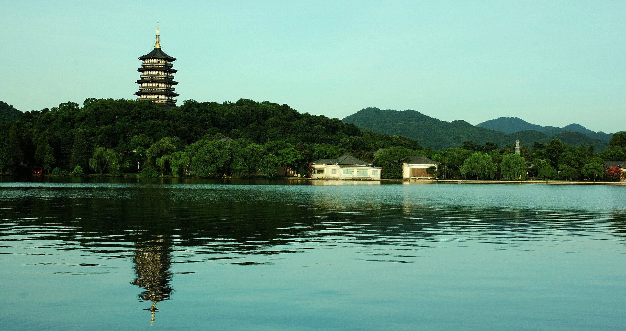 杭州古水鄉 壁紙 — 寧靜的湖面倒映著一座傳統寶塔，矗立於翠綠山丘之巔，天空清澈。
