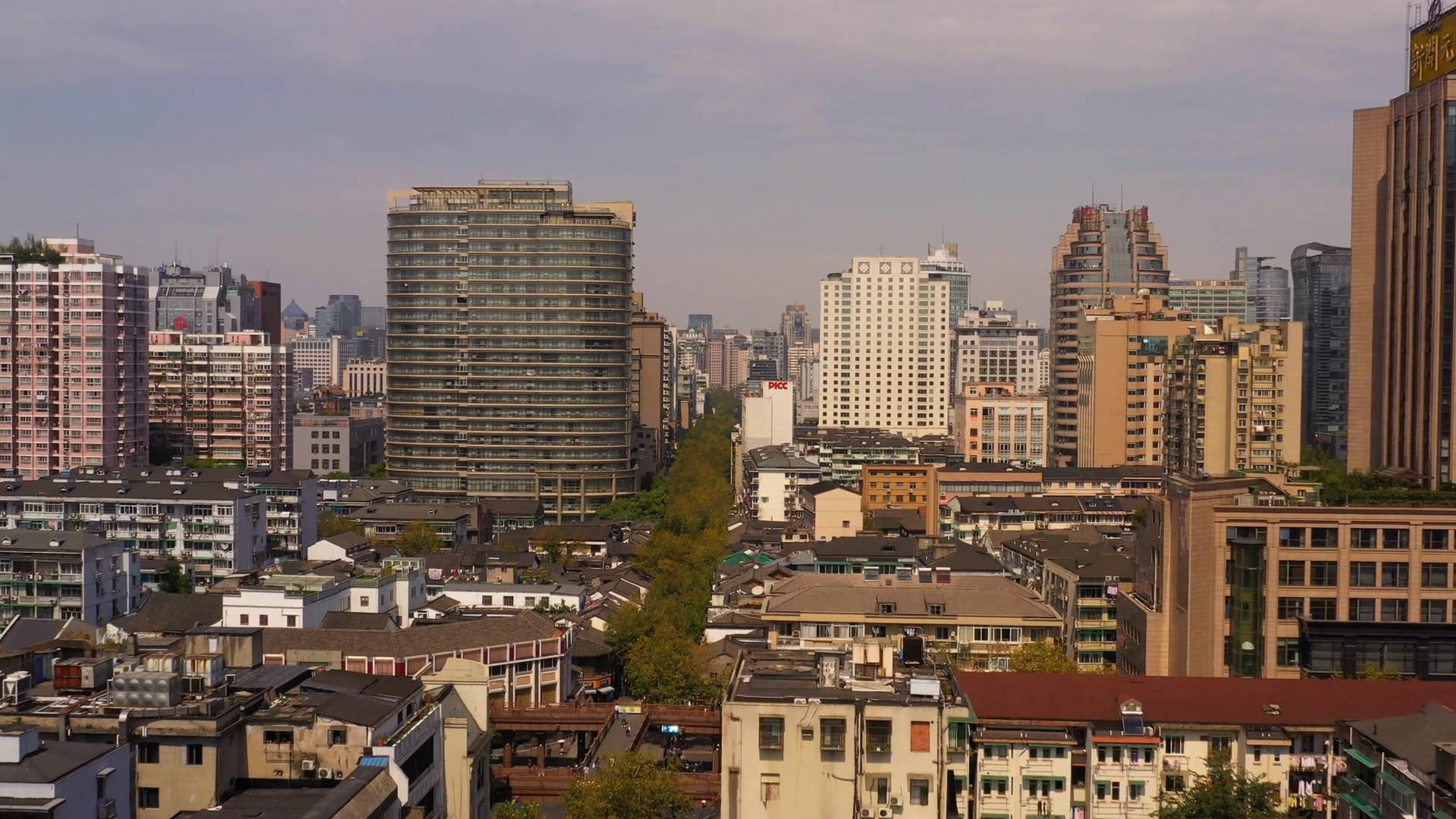杭州西湖絕美風光 壁紙 — 一個密集城市天際線的全景視圖，現代玻璃塔在朦朧天空下聳立於傳統低層建築之上。