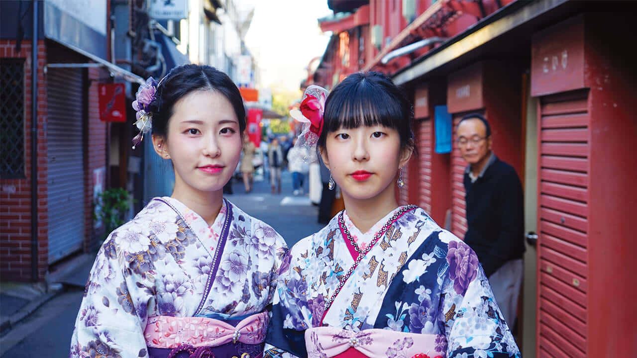 兩位年輕女性穿著色彩繽紛的和服，在狹窄的日本小巷中擺姿勢。