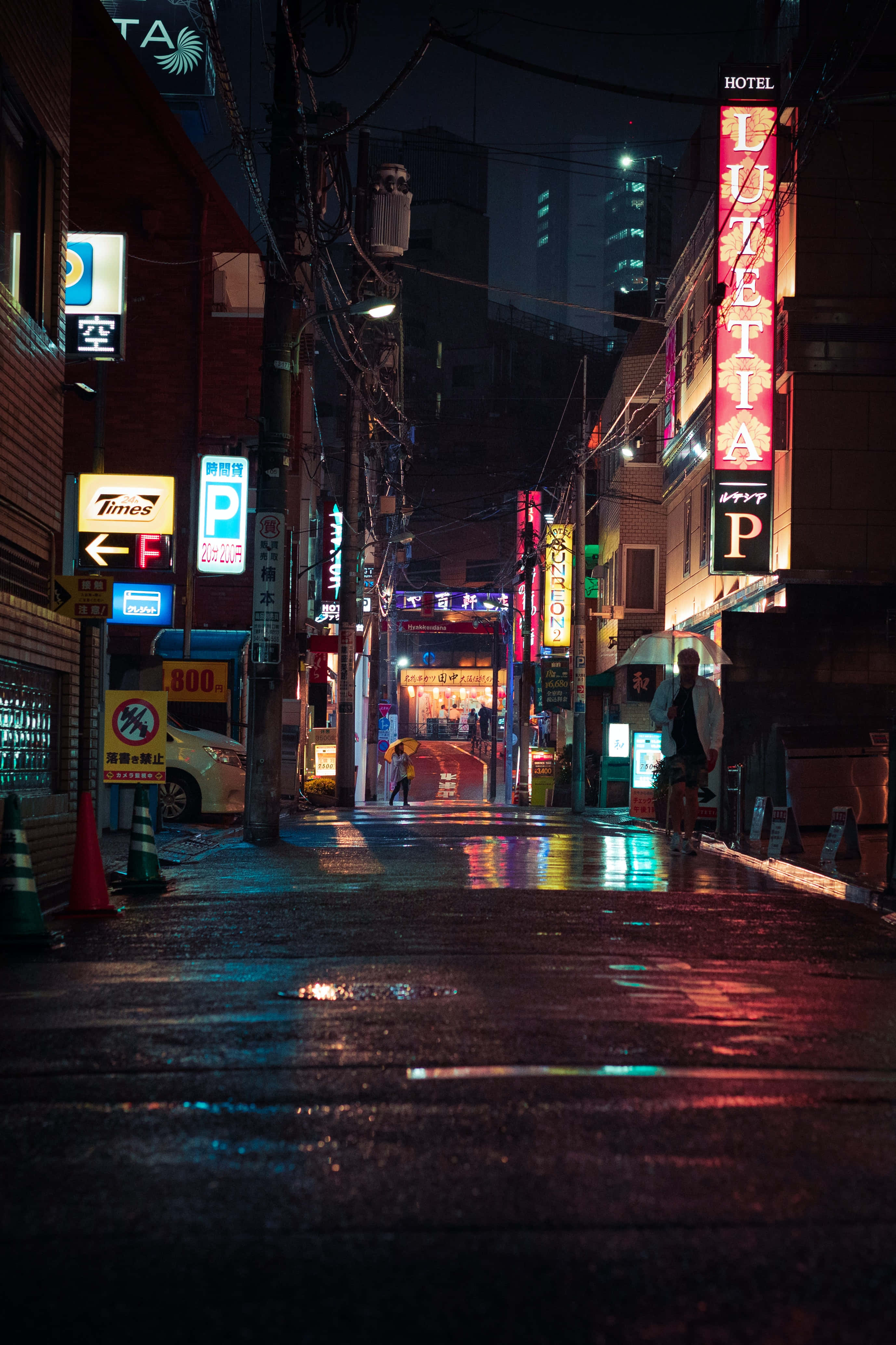 Street 桌布 壁紙 — 東京一條被雨淋濕、霓虹燈閃爍的夜晚小巷，在黑暗的天空下，潮濕的路面反射出鮮豔的招牌。