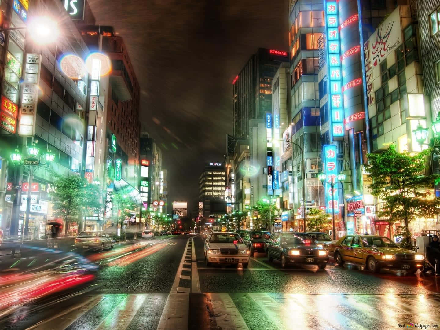 東京光澤都市街景背景 壁紙 — 一條充滿活力的東京霓虹燈街道夜景，車燈在濕漉漉的路面上留下光跡。