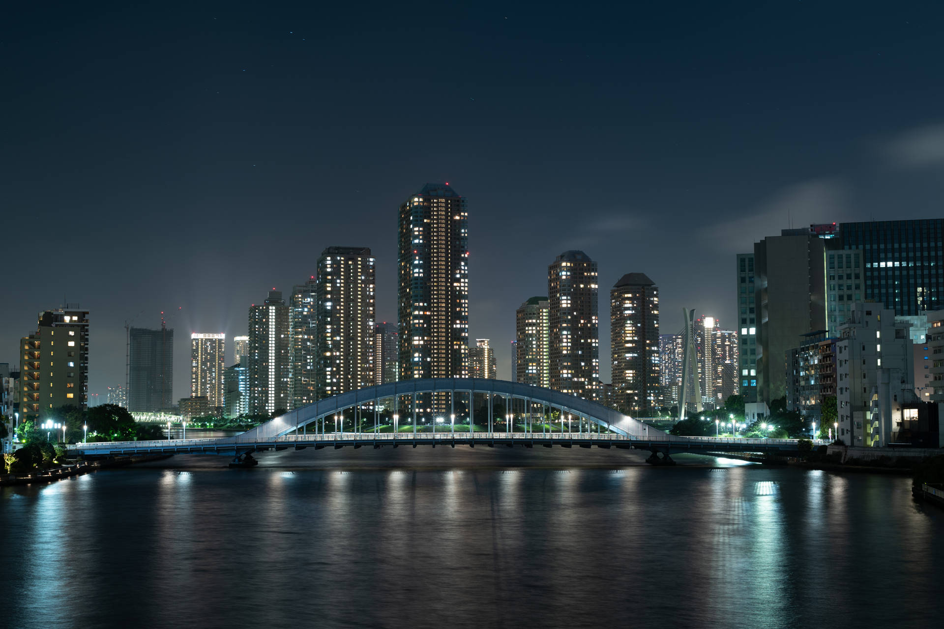 夜間水面上的一座亮燈橋樑，背景有城市建築。