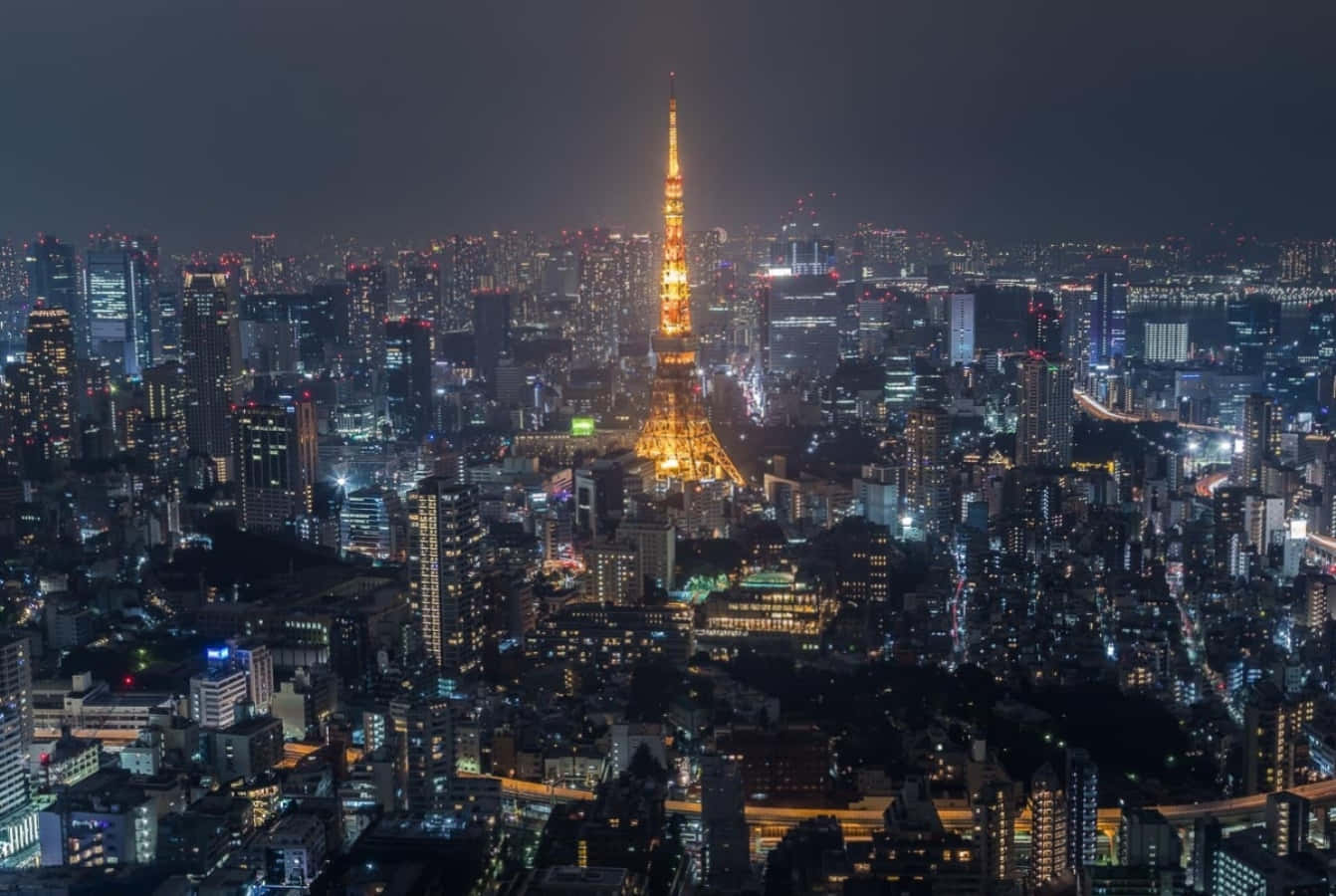 東京 桌布 壁紙 — 東京塔在黑暗的天空中閃耀著金色光芒，城市的燈光照亮了下方廣闊的城市景觀。