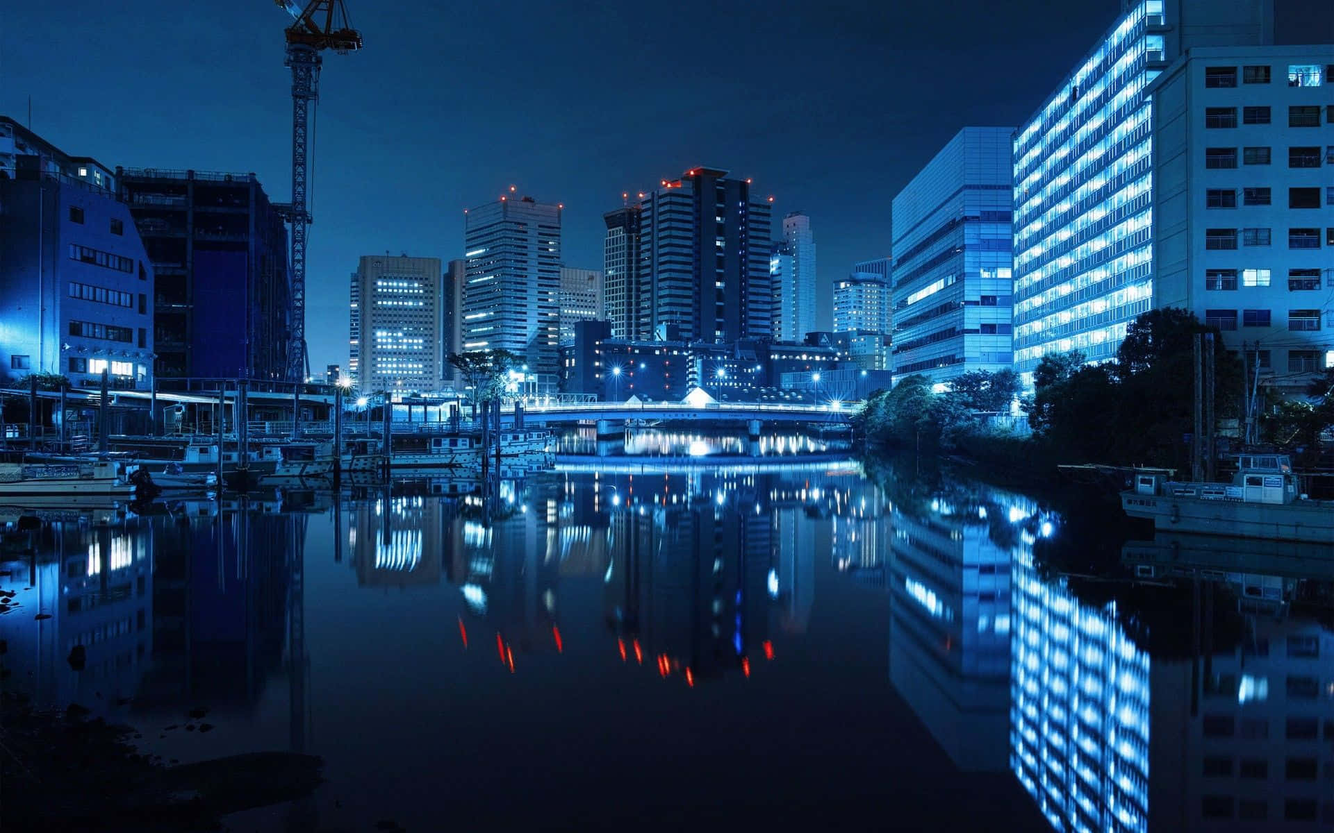 東京夜景深藍效果 壁紙 — 寧靜的夜景，閃爍的摩天大樓和一條平靜的河流反射出它們的藍色和白色燈光。
