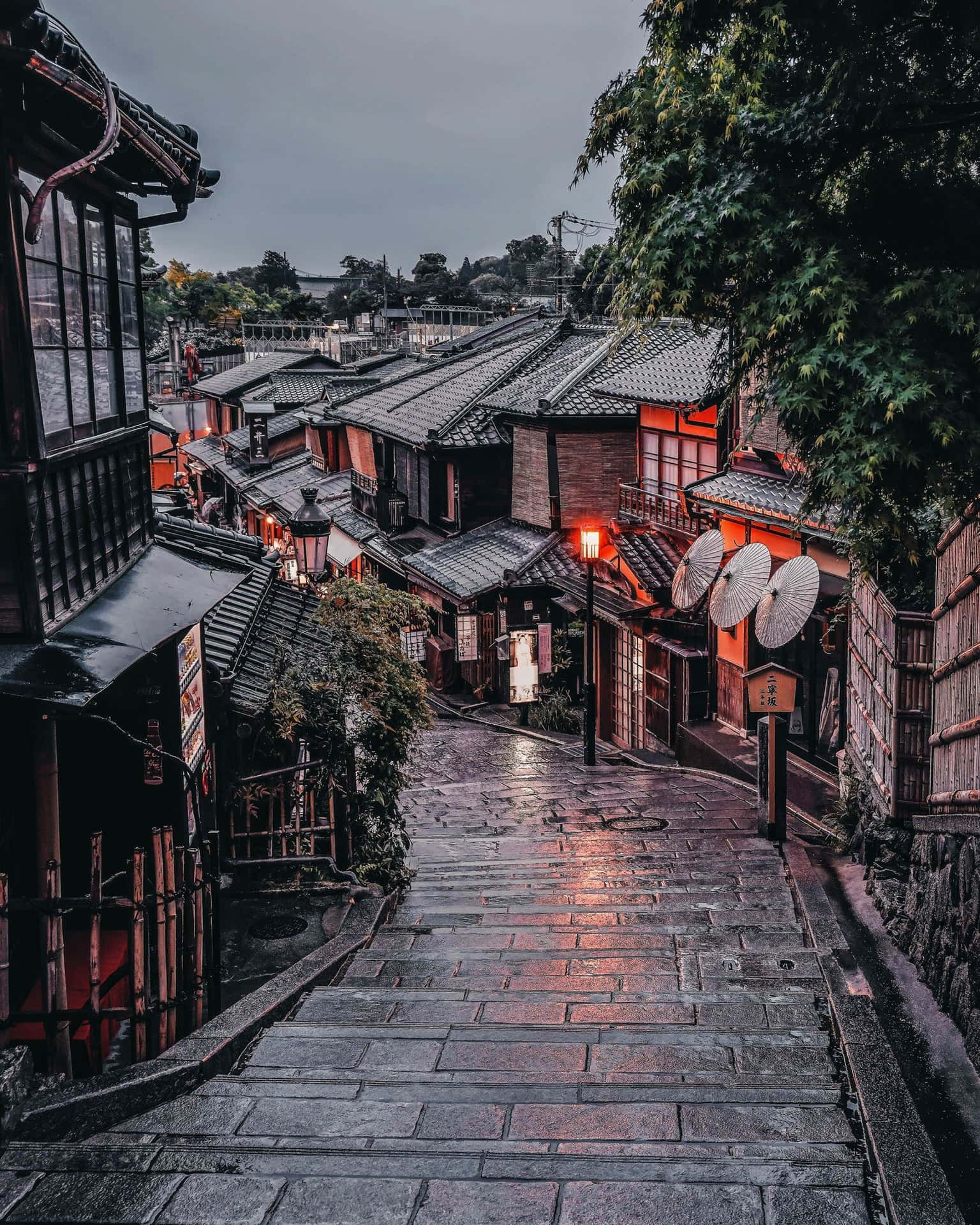 濕滑的石階沿著一條狹窄的日本街道向上延伸，兩旁是傳統木建築，被溫暖的燈籠照亮。
