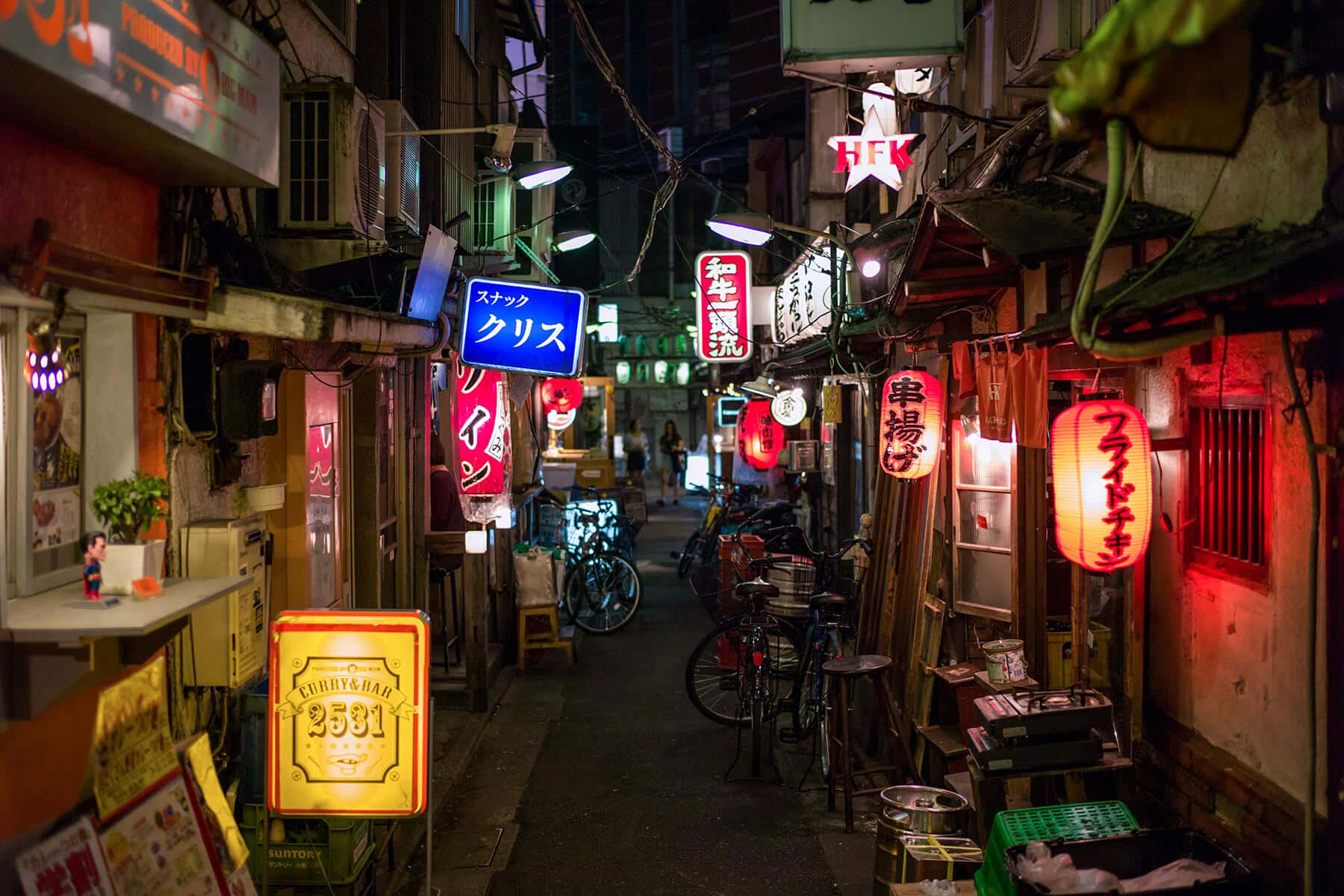 夜晚東京狹窄小巷，被霓虹招牌和紅色燈籠照亮，單車停泊在牆壁旁。