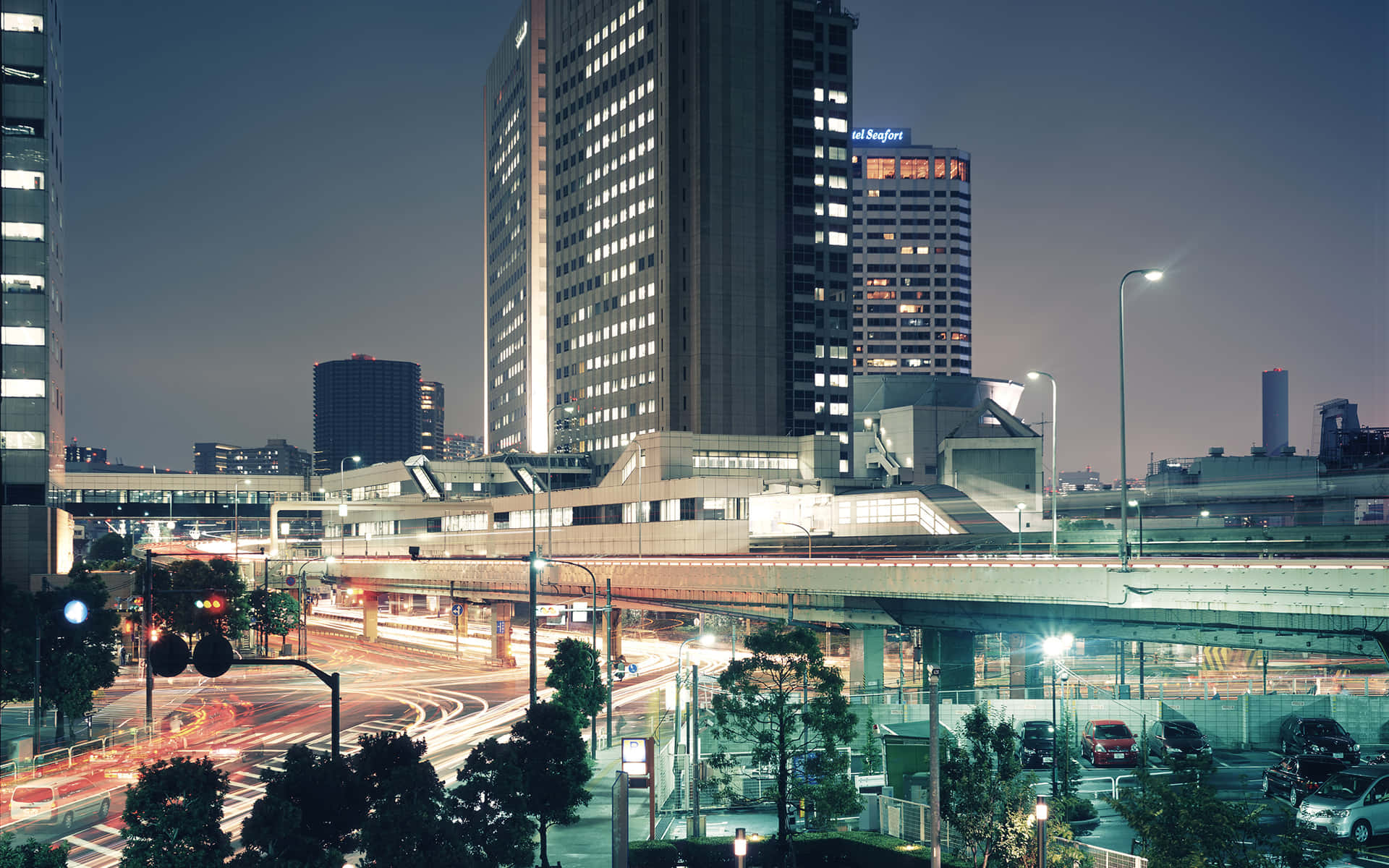 東京未來主義建築背景 壁紙 — 黃昏時分充滿活力的城市景觀，閃爍的摩天大樓和高架公路上汽車燈光的條紋。