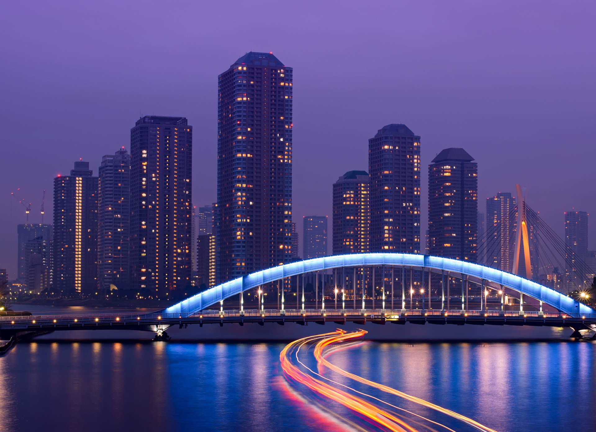 夜晚水上藍色燈光橋樑，帶有汽車燈光軌跡和城市建築。