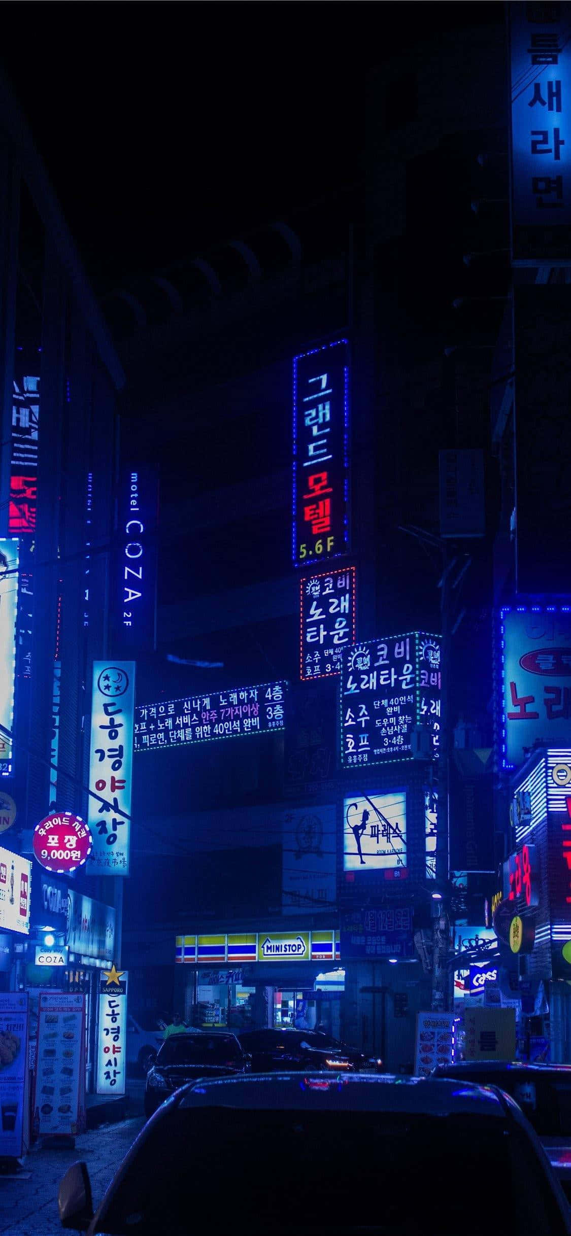 東京的璀璨夜晚 壁紙 — 韓國城市夜晚一條狹窄的霓虹燈小巷，發光的招牌映照在潮濕的人行道和停泊的汽車上。
