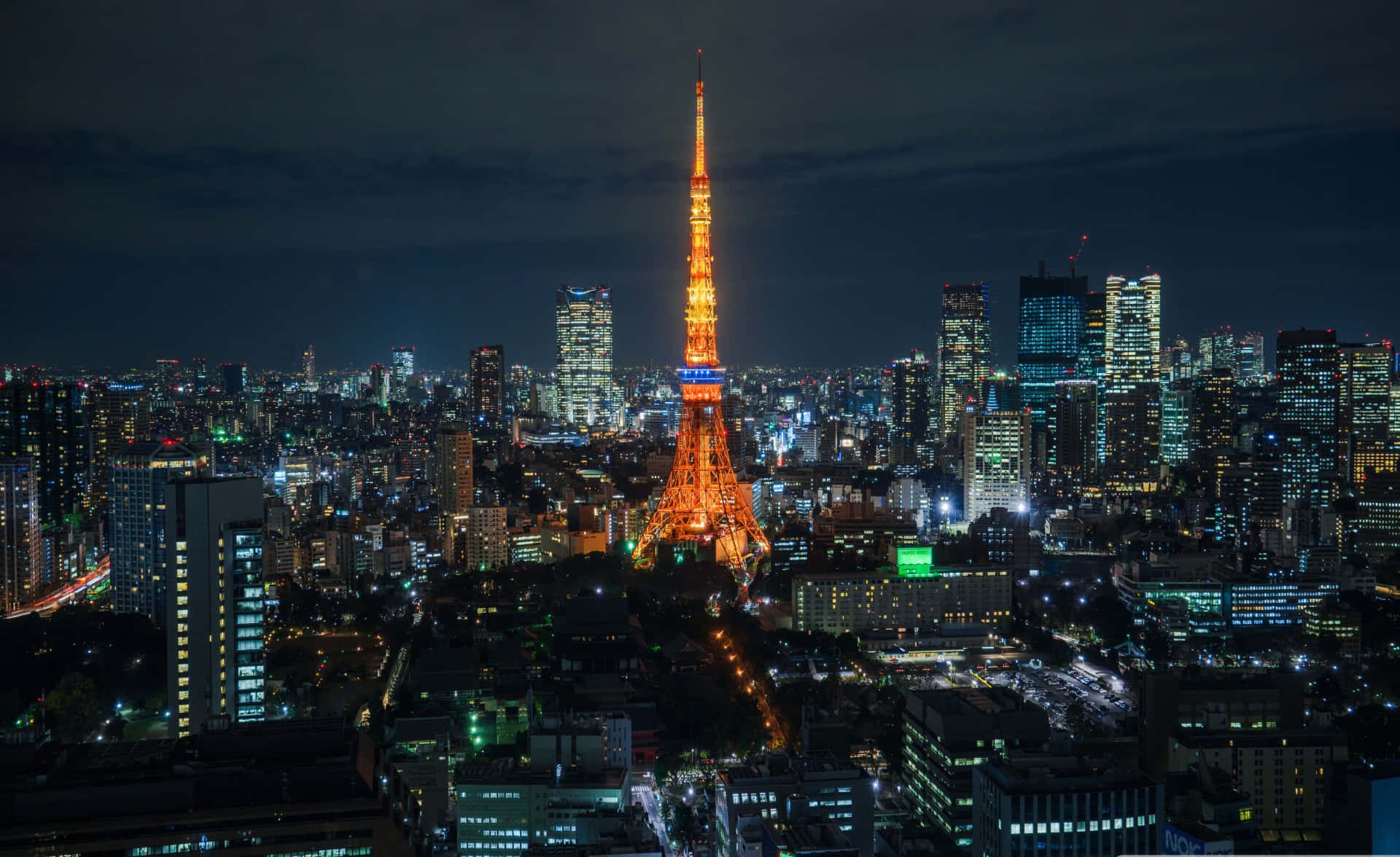 東京背景 亮黃色東京塔 壁紙 — 東京鐵塔在漆黑的天空中散發溫暖的光芒，城市的燈光照亮了下方廣闊的城市景觀。