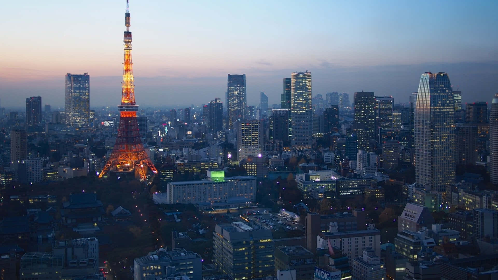 東京背景 城市間的亮麗東京塔 壁紙 — 東京塔在暮色中溫暖地發光，城市燈光在黃昏時分閃爍於都市天際線。