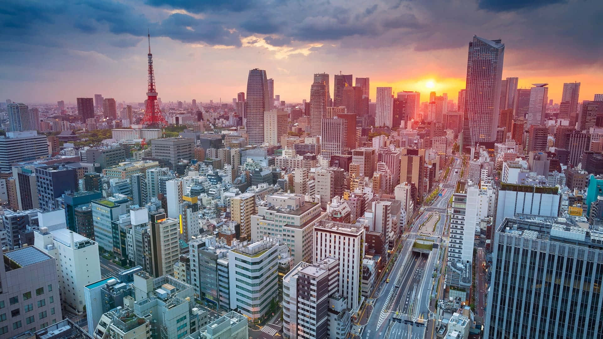 東京背景 日落時分的東京 壁紙 — 日落時分東京天際線的鳥瞰圖，塔橋在橙色雲層和密集的城市建築中閃耀。