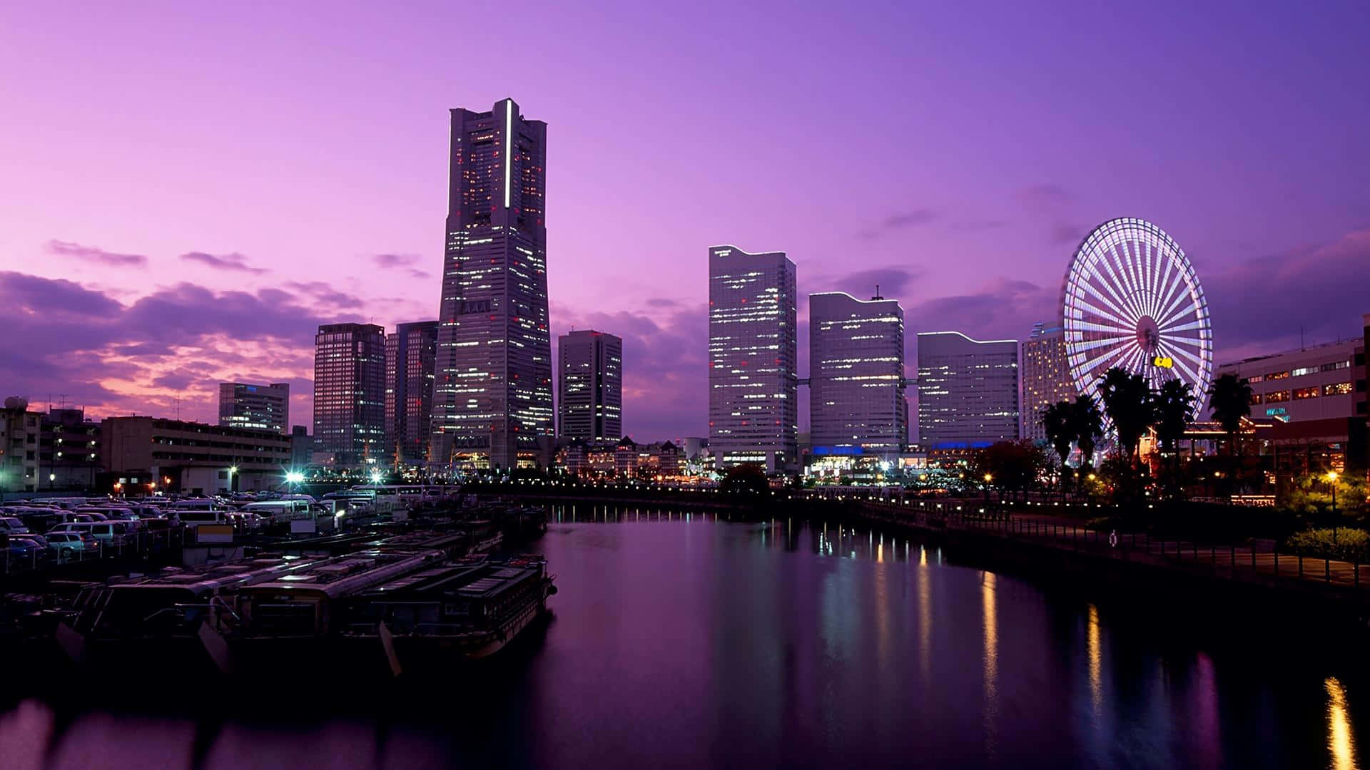 東京背景 河畔城市燈光 壁紙 — 充滿活力的紫色暮色城市景觀，發光的摩天大樓和摩天輪倒映在平靜的水面上。