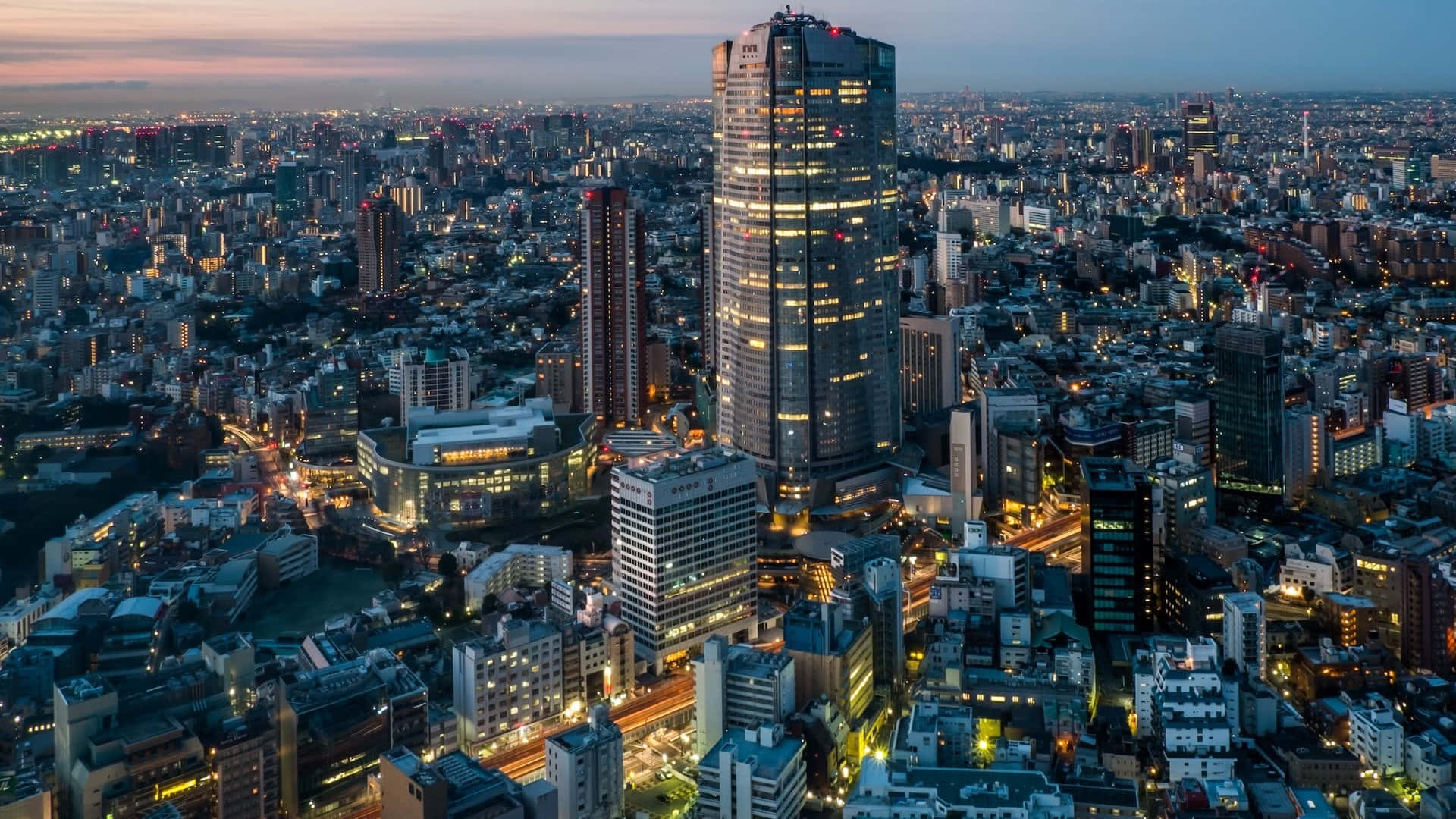 東京背景 涉谷之森摩理塔 壁紙 — 黃昏時分廣闊城市景觀的鳥瞰圖，一座高聳的摩天大樓在暮色天空中閃耀。