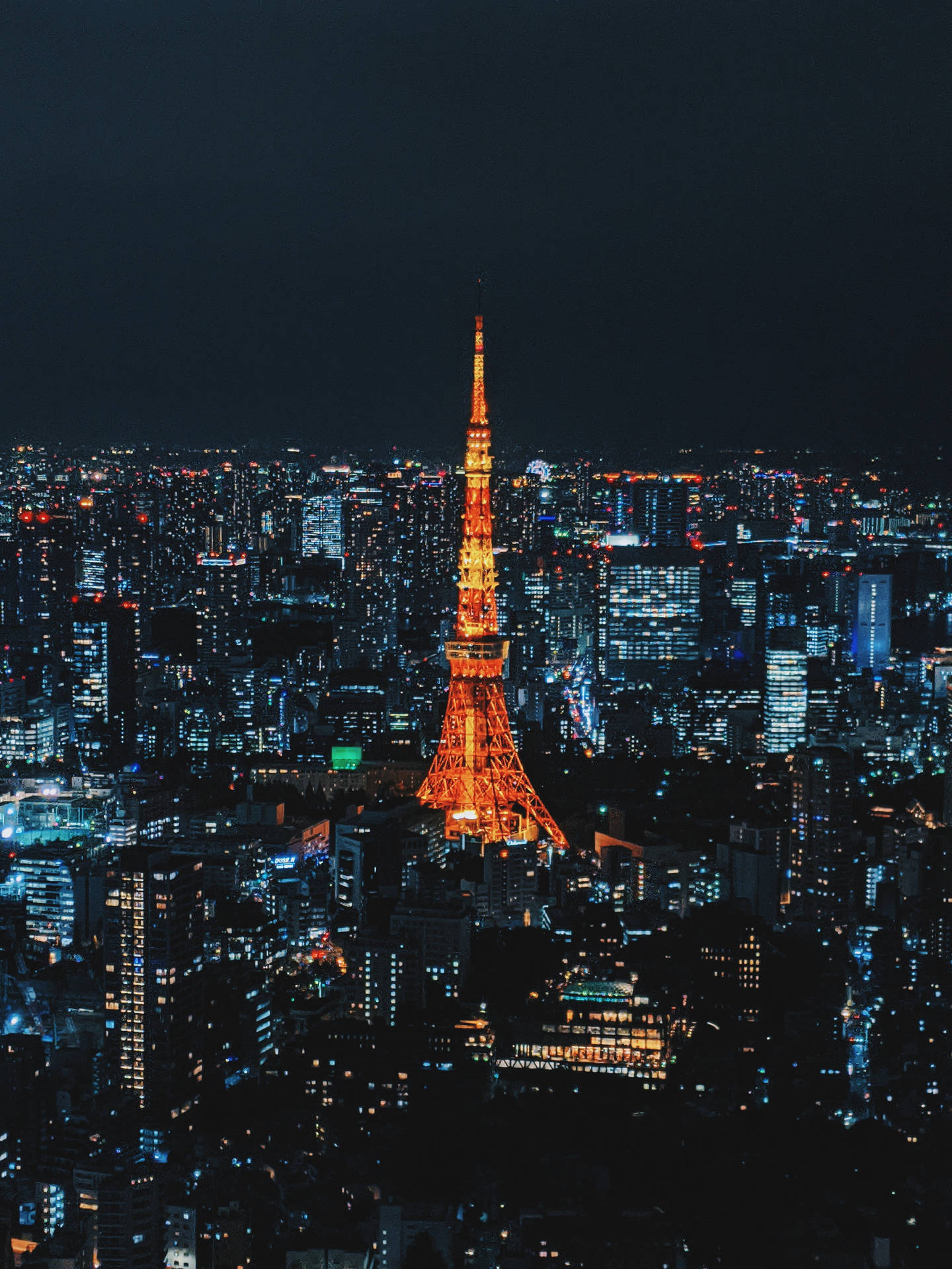 東京鐵塔橙黃燈光夜景 壁紙 — 東京塔在漆黑的天空中散發溫暖的光芒，下方是無數藍色和白色燈光照亮的廣闊城市景觀。