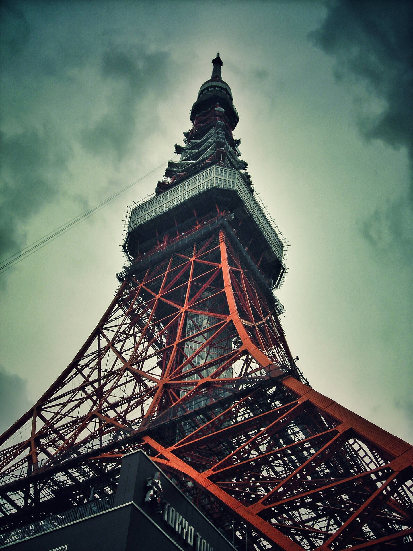 東京鐵塔陰雲密布天際 壁紙 — 從低角度觀看東京鐵塔的紅色鋼鐵格子結構刺穿陰沉多雲的天空。
