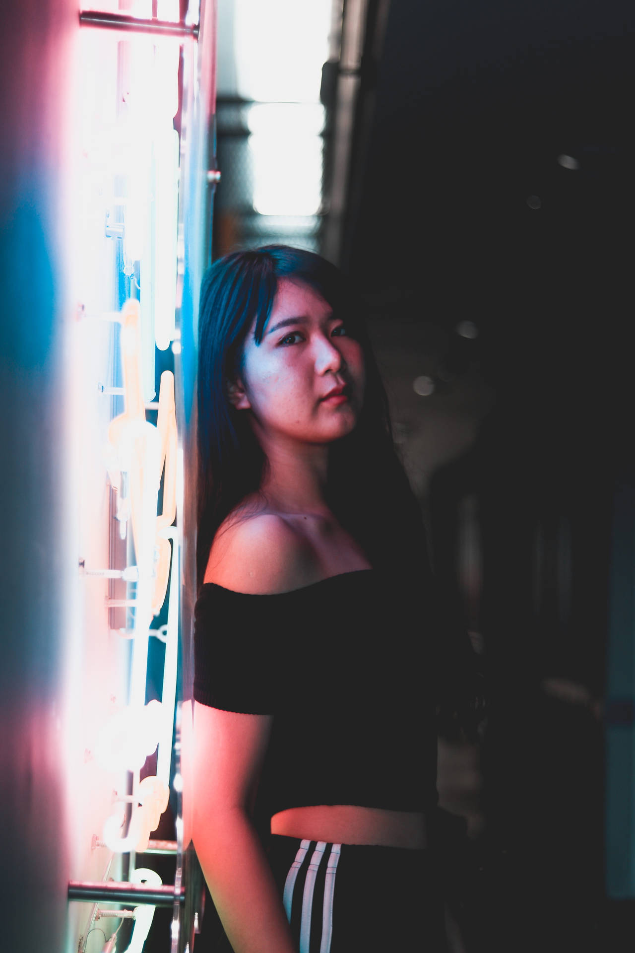 年輕女性站在黑暗城市小巷中發光的霓虹燈牌旁。