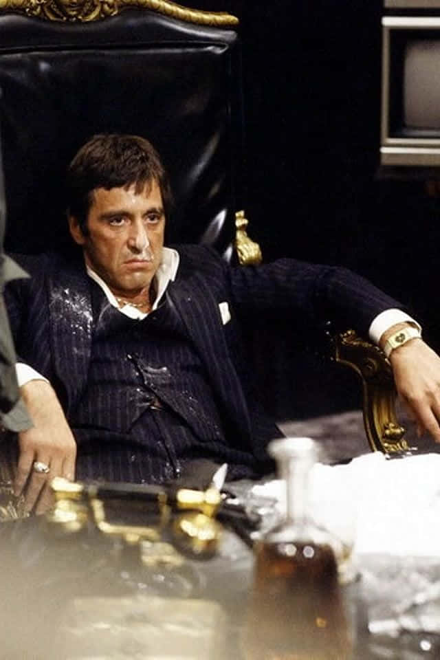 一個穿著細條紋西裝的男人坐在一張帶有金色邊飾的黑色皮革椅上，神情專注。