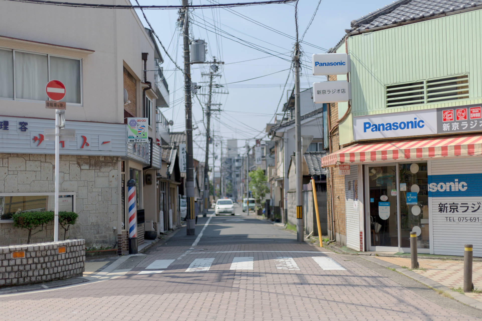一條寧靜的日本城市街道，有商店和電線，上方是晴朗的天空。