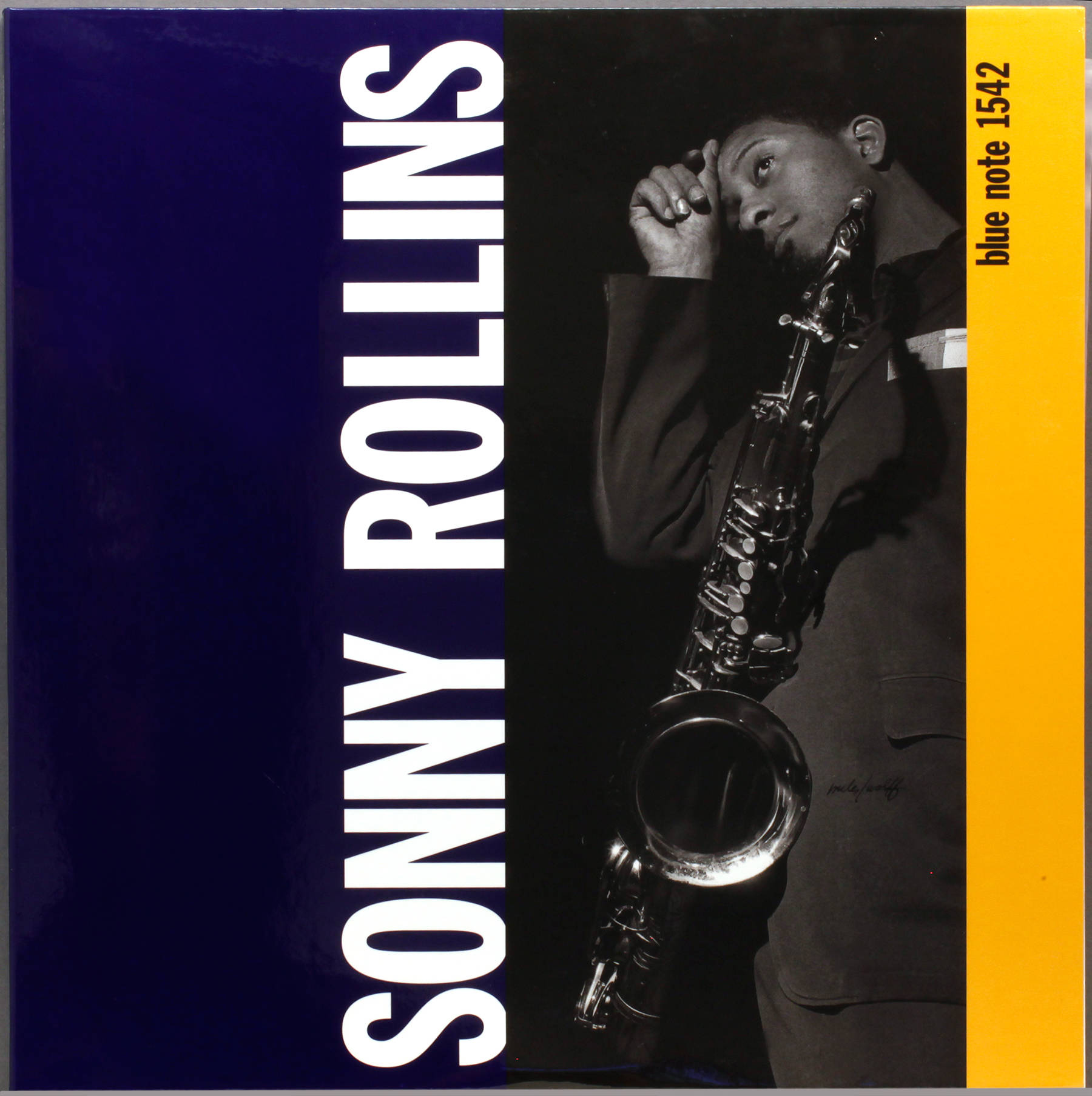 松尼·羅林斯《Blue Note Edition》專輯封面 壁紙 — 一張黑白肖像，爵士薩克斯風手 Sonny Rollins 在深色背景前手持樂器，背景帶有醒目的藍色和黃色圖形元素。