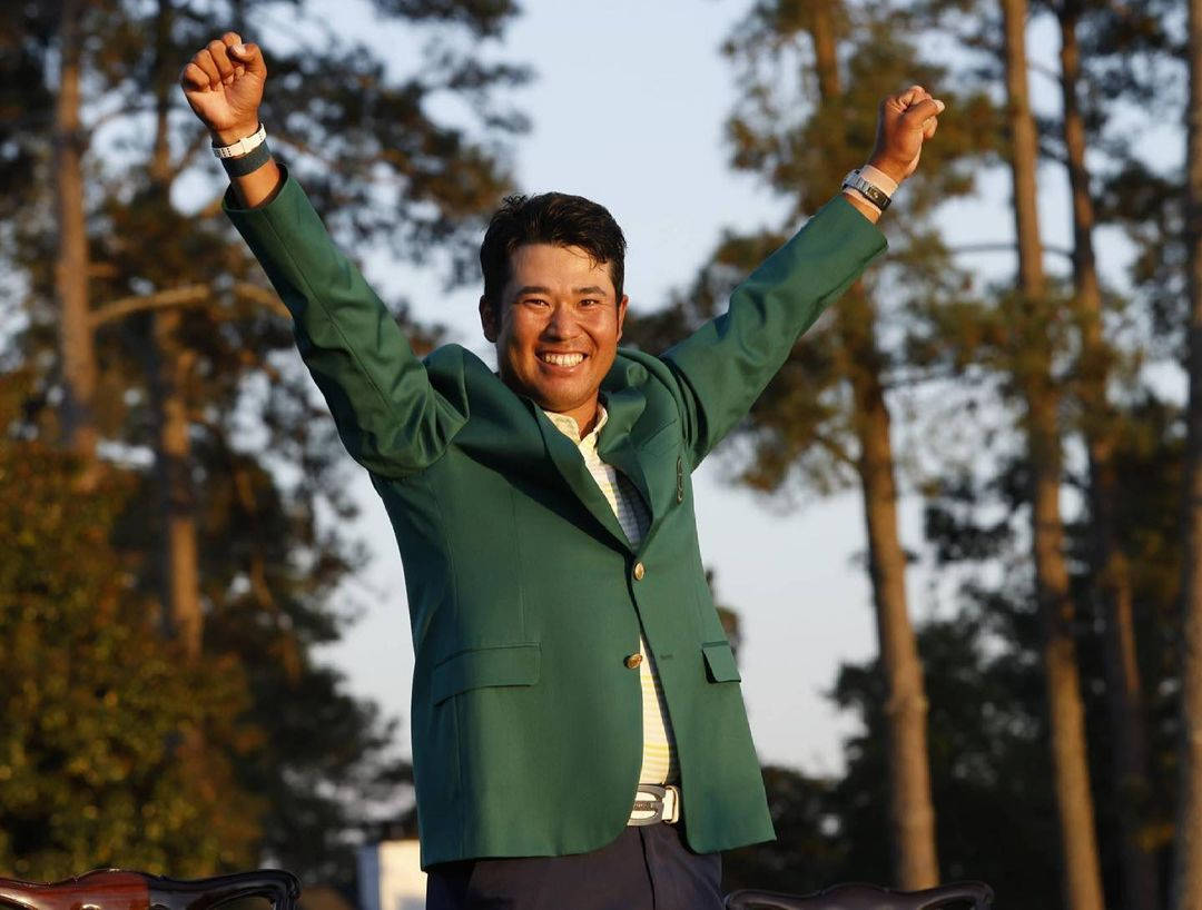 身穿綠色外套的高爾夫球手在戶外舉起雙臂慶祝勝利。