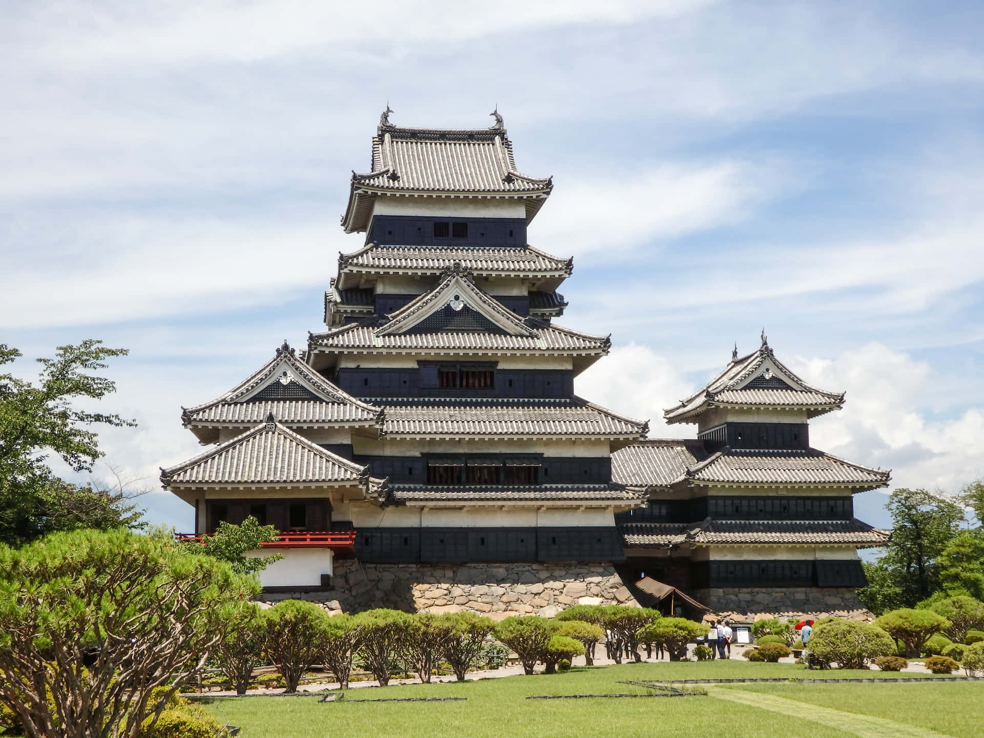 松本城五層外觀 壁紙 — 一座雄偉的多層日本城堡，擁有深色木牆和灰色瓦片屋頂，在藍天白雲下高高聳立。