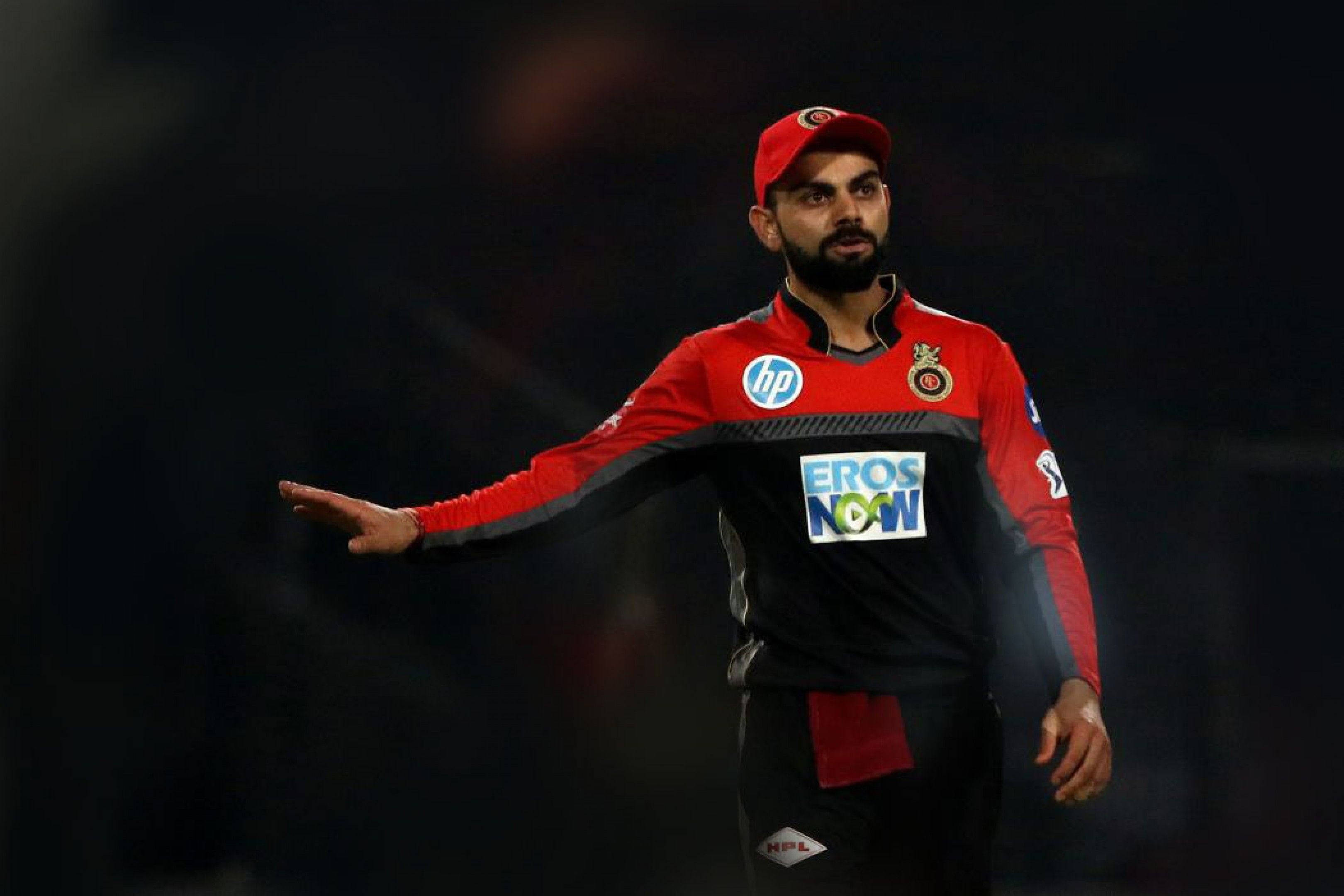 virat kohli rcb 桌布 壁紙 — 板球運動員維拉·高利（Virat Kohli）戴紅色帽子和球衣，在體育場燈光下的夜間比賽中做手勢。