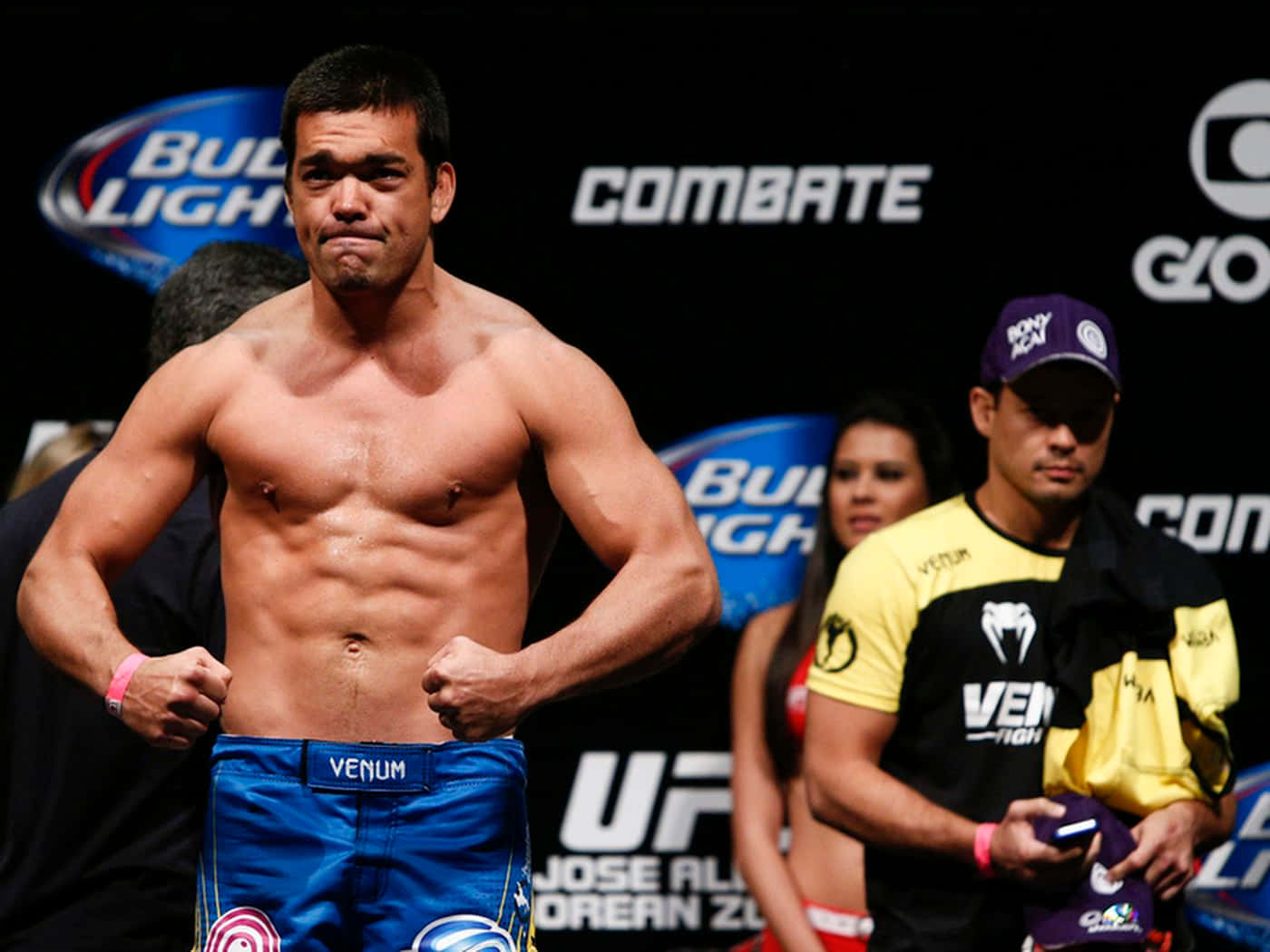 一位赤裸上身的男性MMA拳手穿著藍色短褲在稱重活動中擺姿勢。