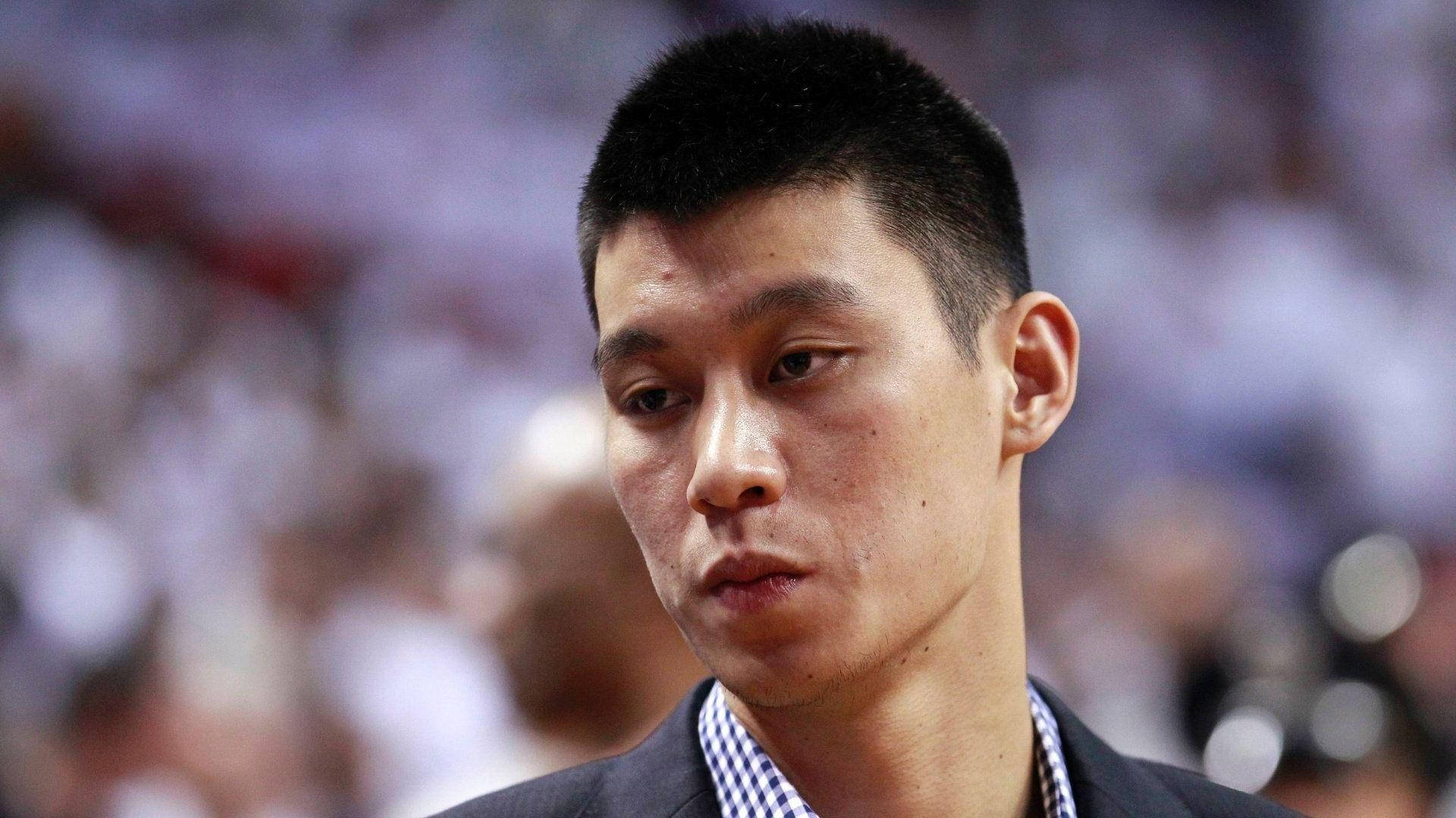 籃球運動員身穿西裝，在競技場中向下看，背景是模糊的人群。