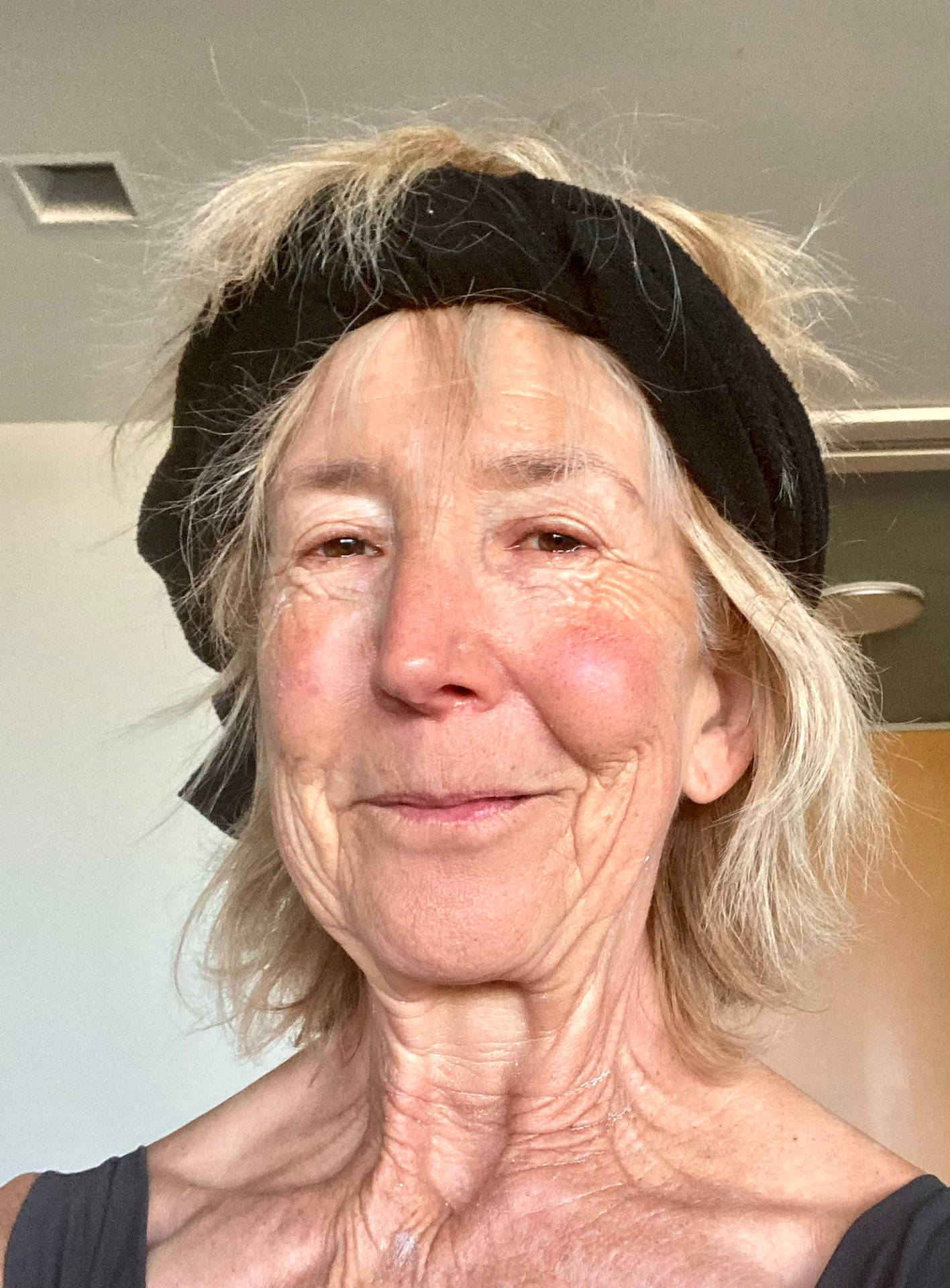 一位微笑的年長女性，金髮，戴黑色頭帶，室內拍攝。