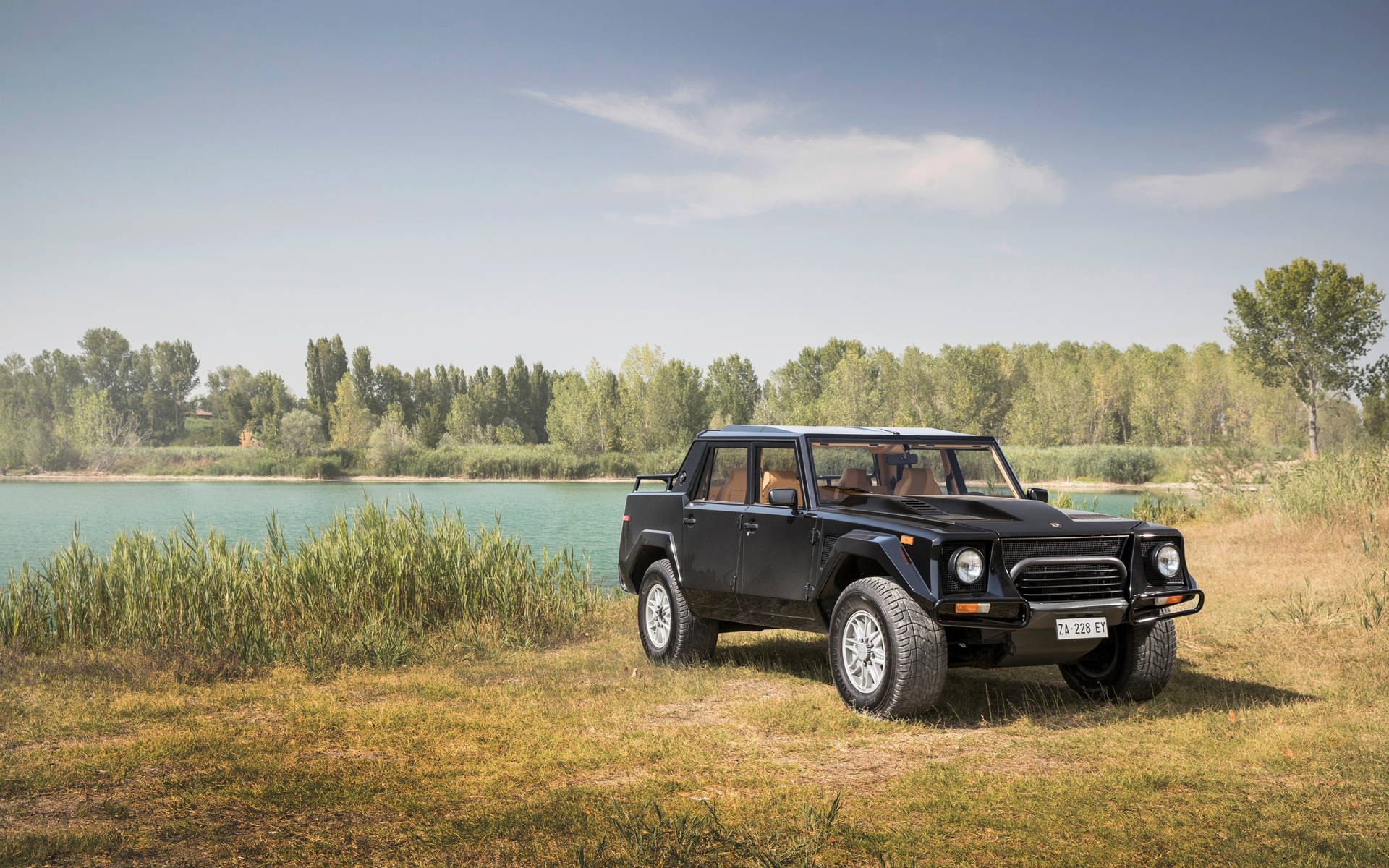 黑色林寶堅尼 LM002 SUV 停泊在湖邊，有樹木和藍天。