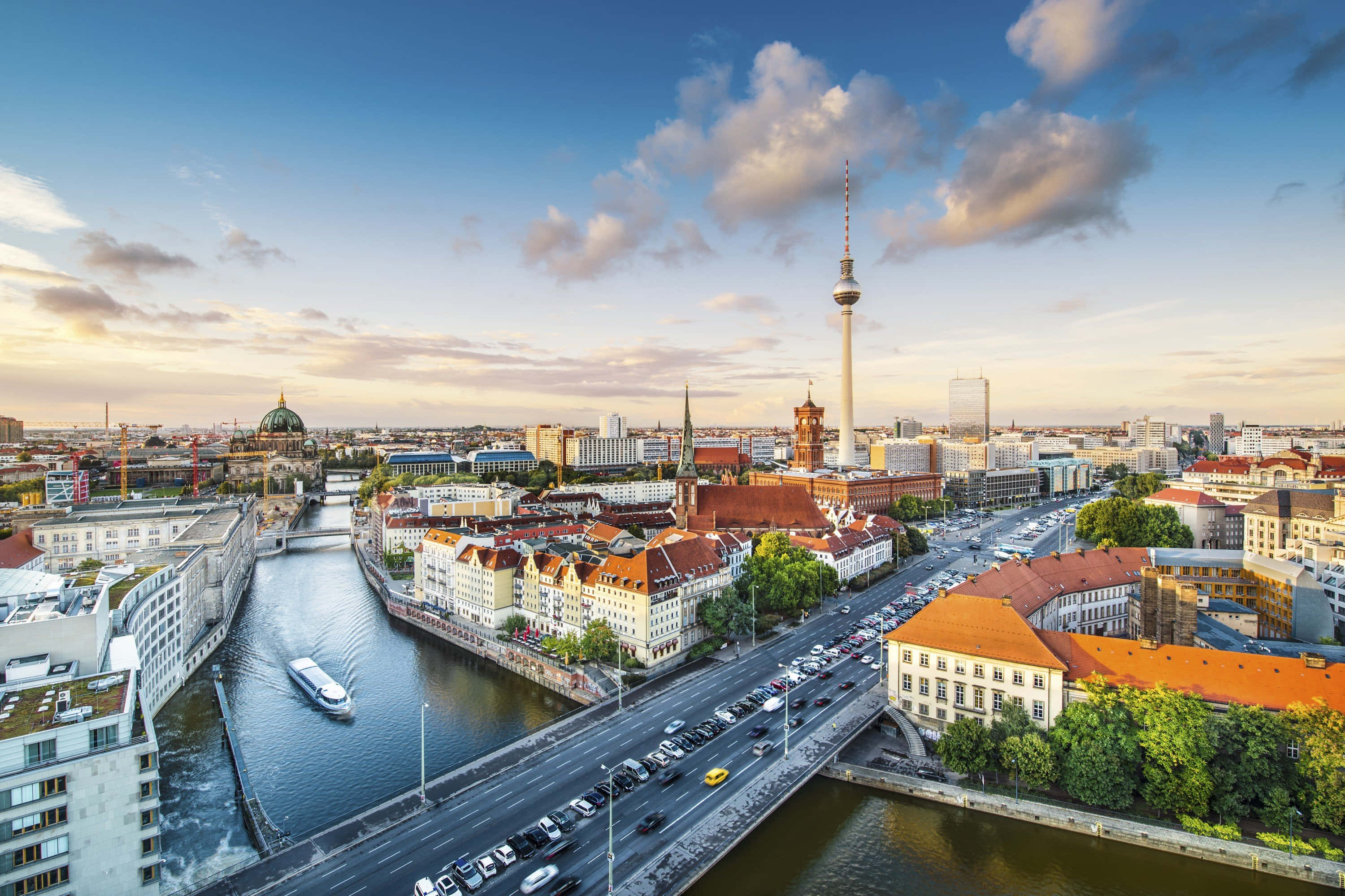 Germany 桌布 壁紙 — 柏林日落時分的鳥瞰圖，電視塔、河船和歷史建築在部分多雲的天空下。